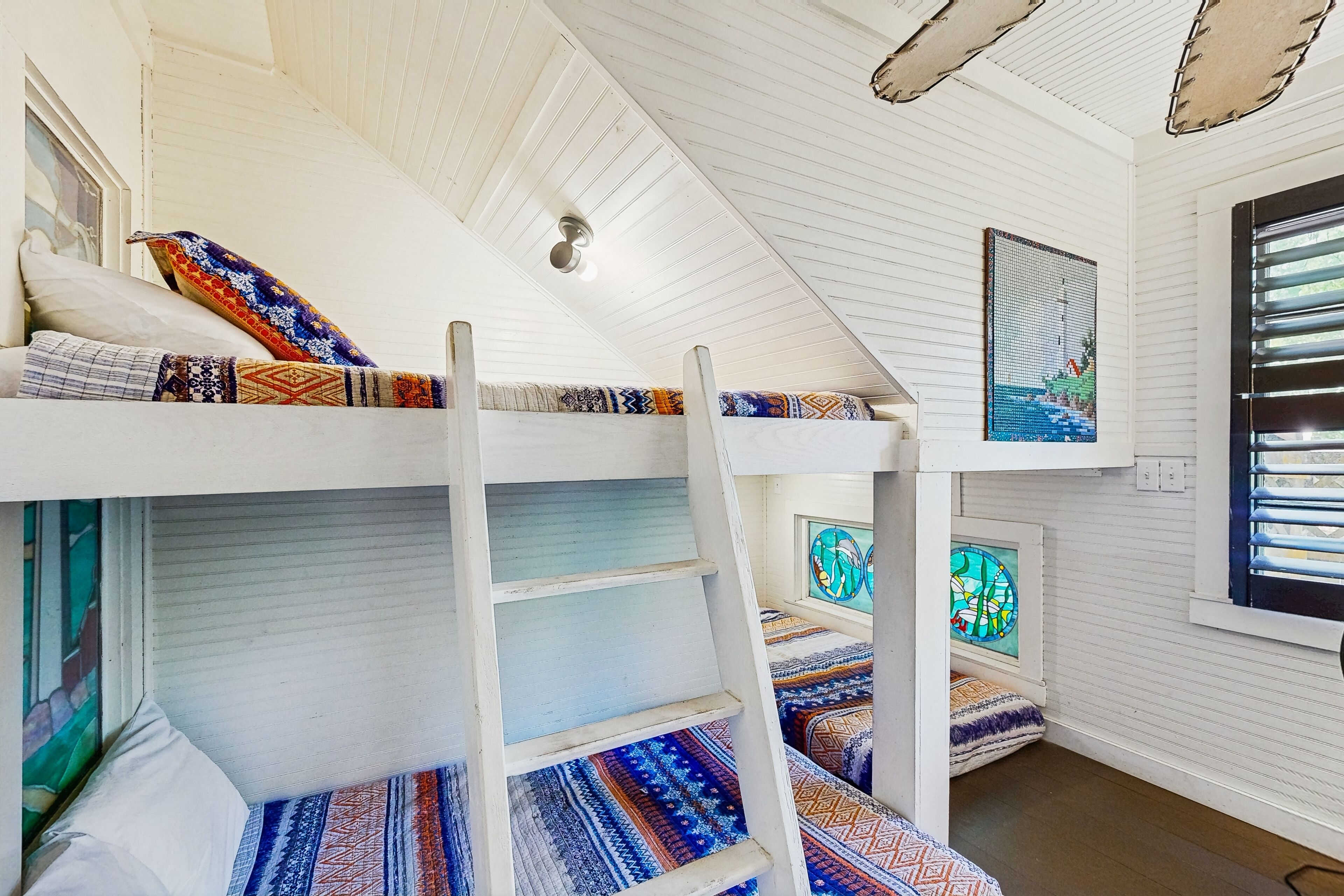 A bunk bed room with a ladder, patterned bedding, and a window with blinds.
