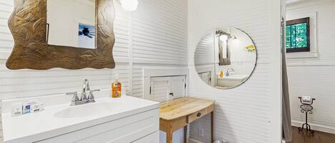 Un baño con un tocador blanco, un taburete de madera, un espejo redondo y un marco de espejo con motivos de peces.