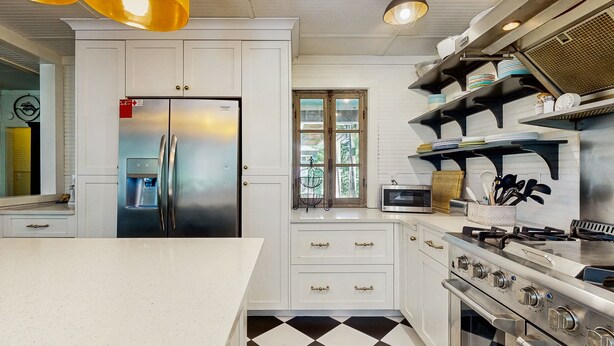 A kitchen with white cabinets, a stainless steel refrigerator, a gas stove, and a black and white checkered floor. - Dog-friendly Cottage by the Beach With Private Pool, Pool Spa, & Free Wifi (St. Simons Island)