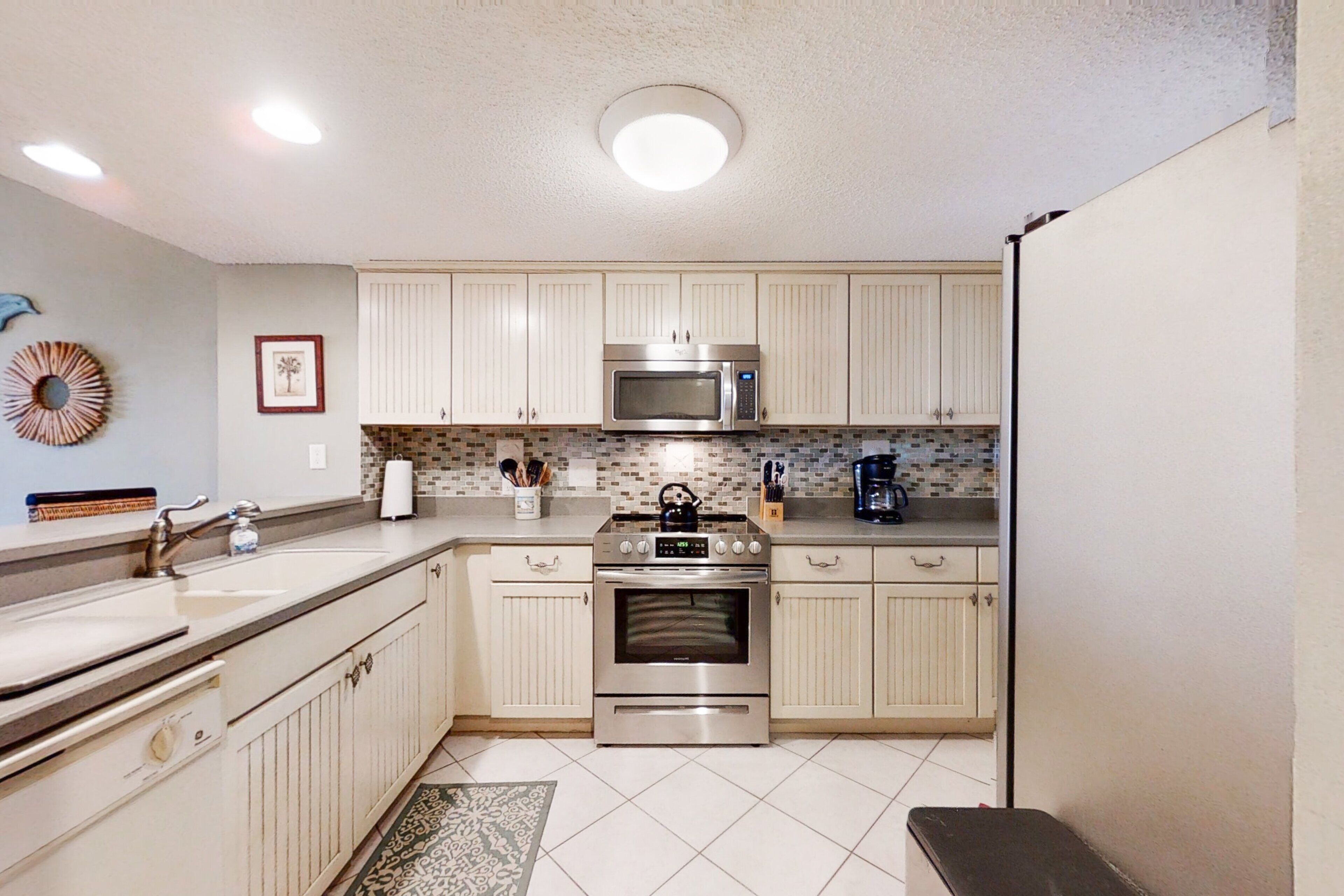 A kitchen with white cabinets, a stainless steel microwave, an oven, a sink, and a coffee maker.