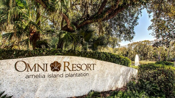 Placa do Omni Resort Amelia Island Plantation, com vegetação exuberante e uma fonte ao fundo.
