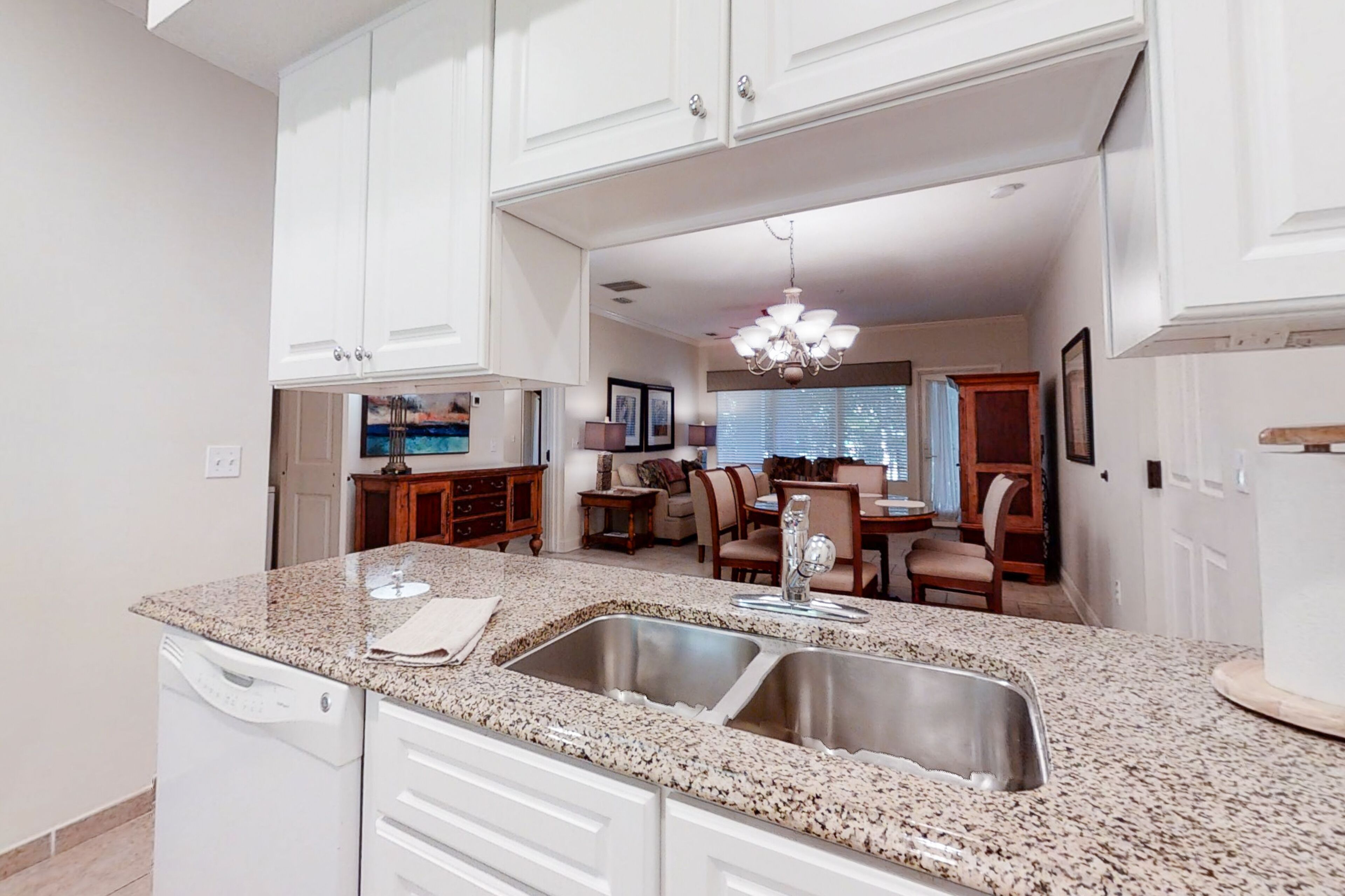 A kitchen with granite countertops, stainless steel sinks, and white cabinetry.