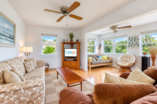 A spacious living room with a sofa, a coffee table, a TV stand, and a ceiling fan. - Dog-friendly Home With Beach Access & Deck - Snowbirds Welcome (St. Augustine)