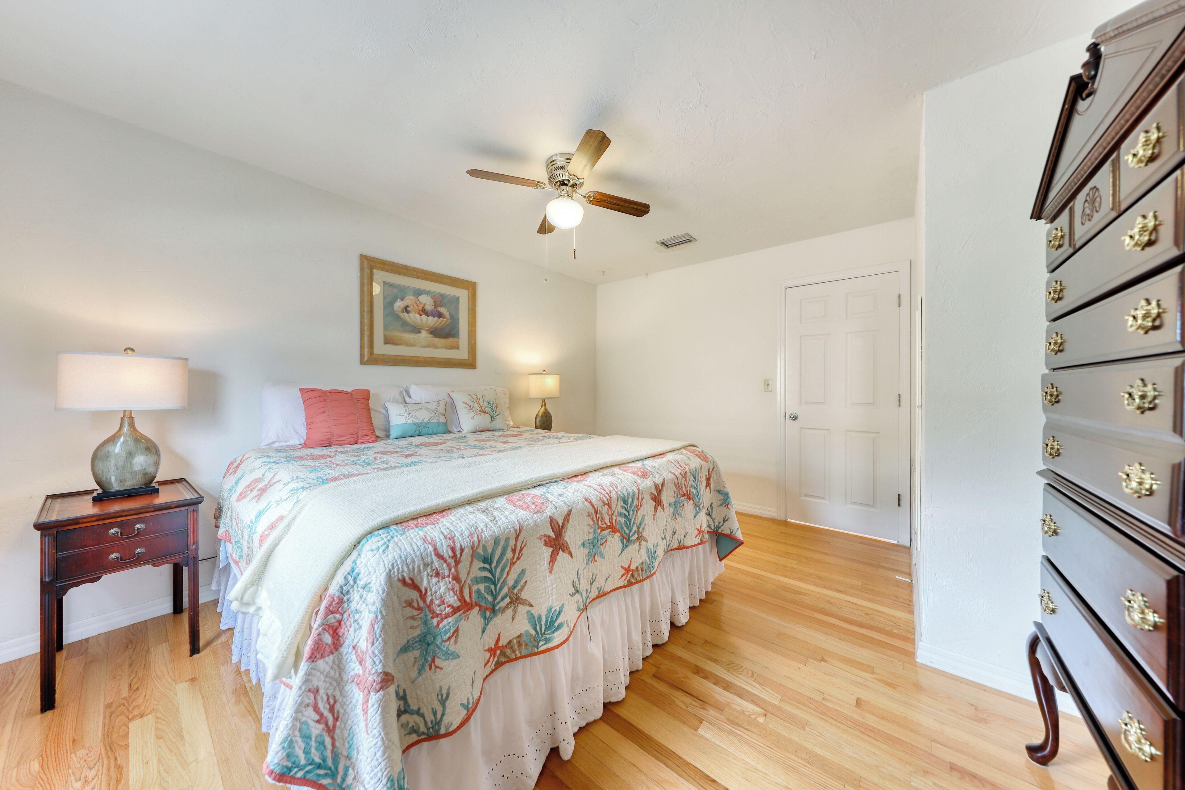 A bedroom with a bed, a ceiling fan, a dresser, and a nightstand.