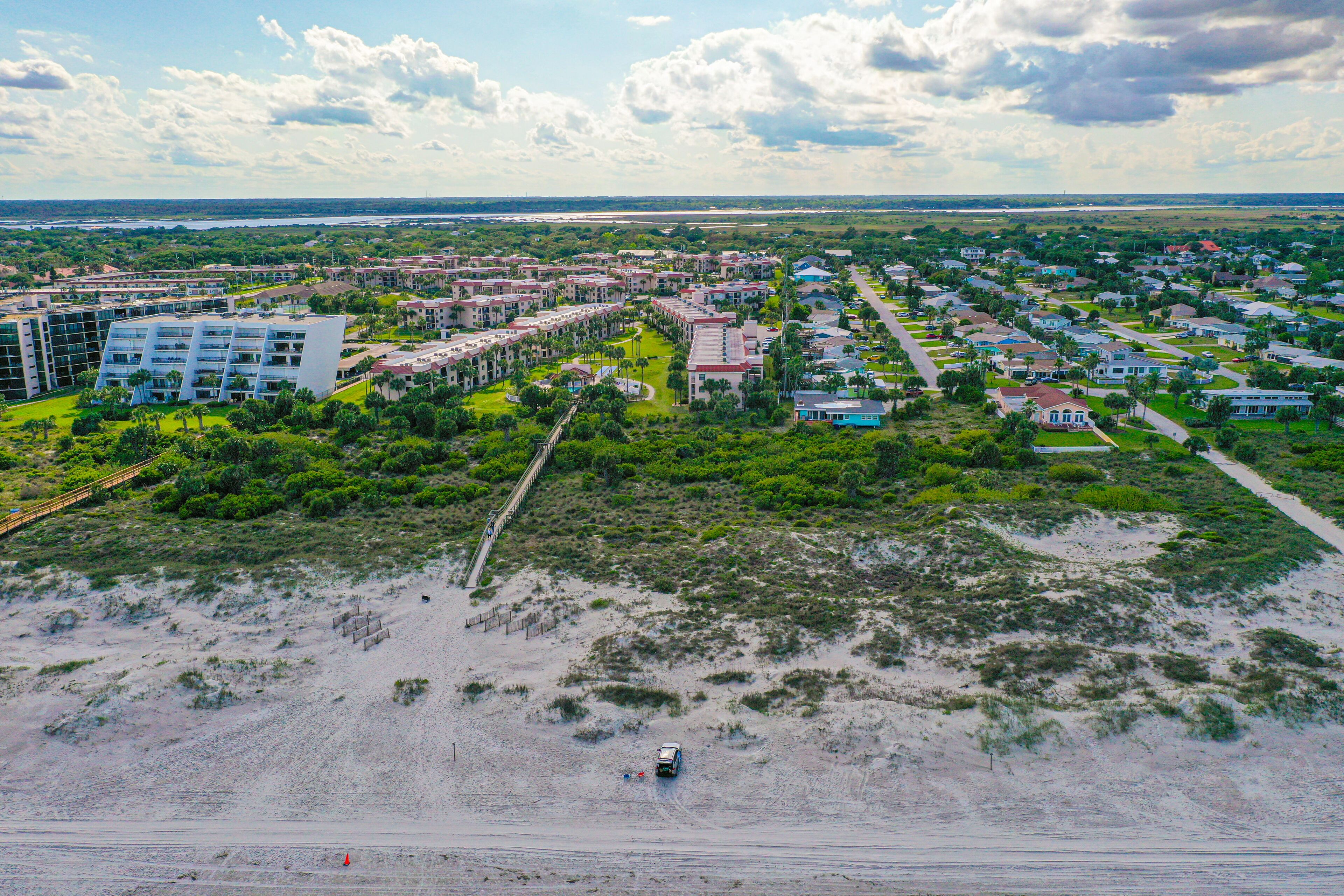 Vista aérea de una zona residencial costera con varios edificios, una playa y un puente.