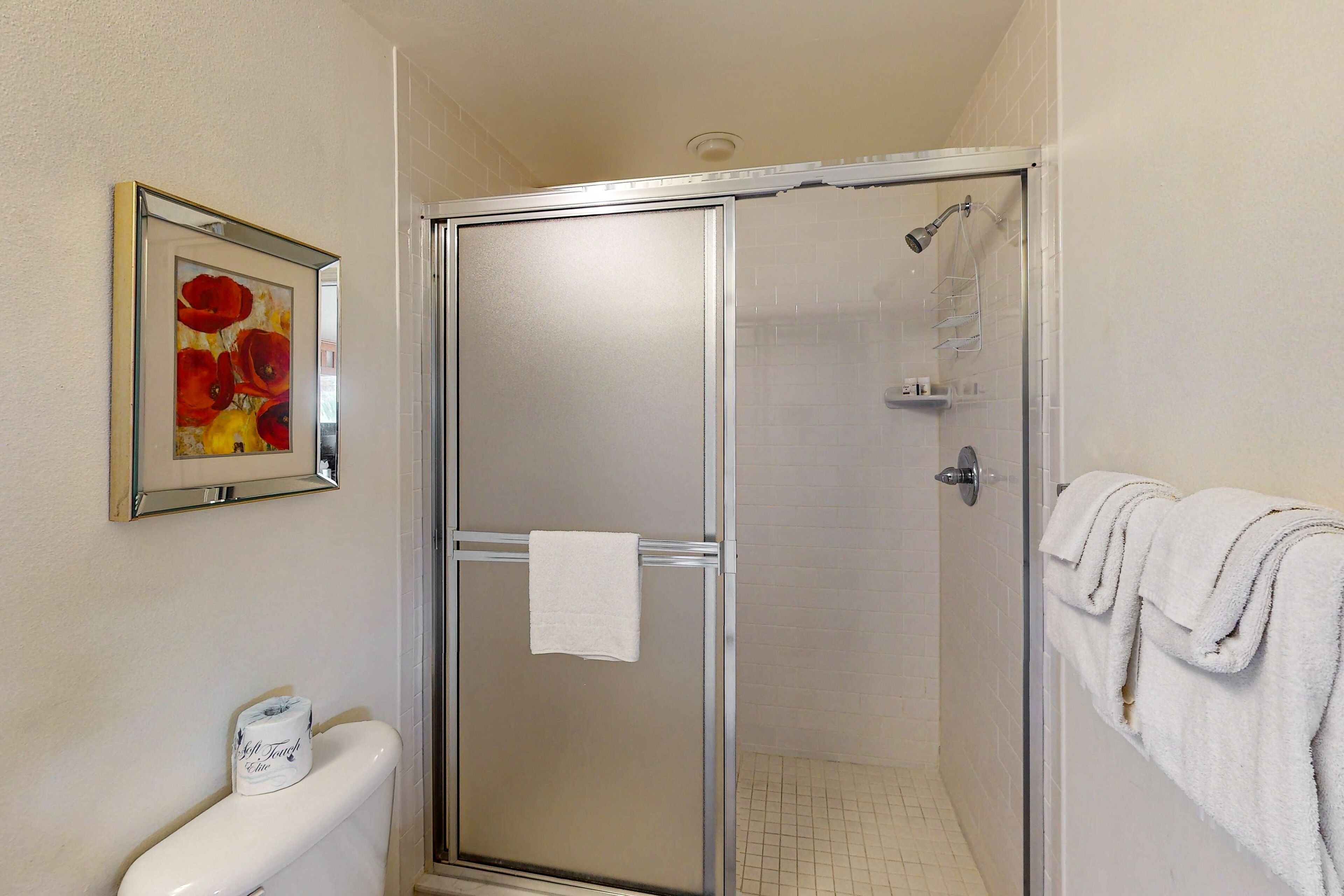 A bathroom with a glass shower enclosure, a toilet, and a framed painting on the wall.