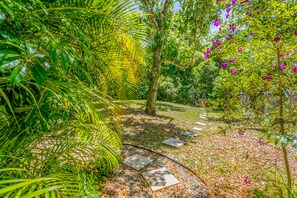 A garden pathway with stone slabs, surrounded by lush greenery and flowering plants. - Dog-friendly Home With High-speed Wifi, Washer/dryer, Central AC, & Adult Bikes (St. Augustine)