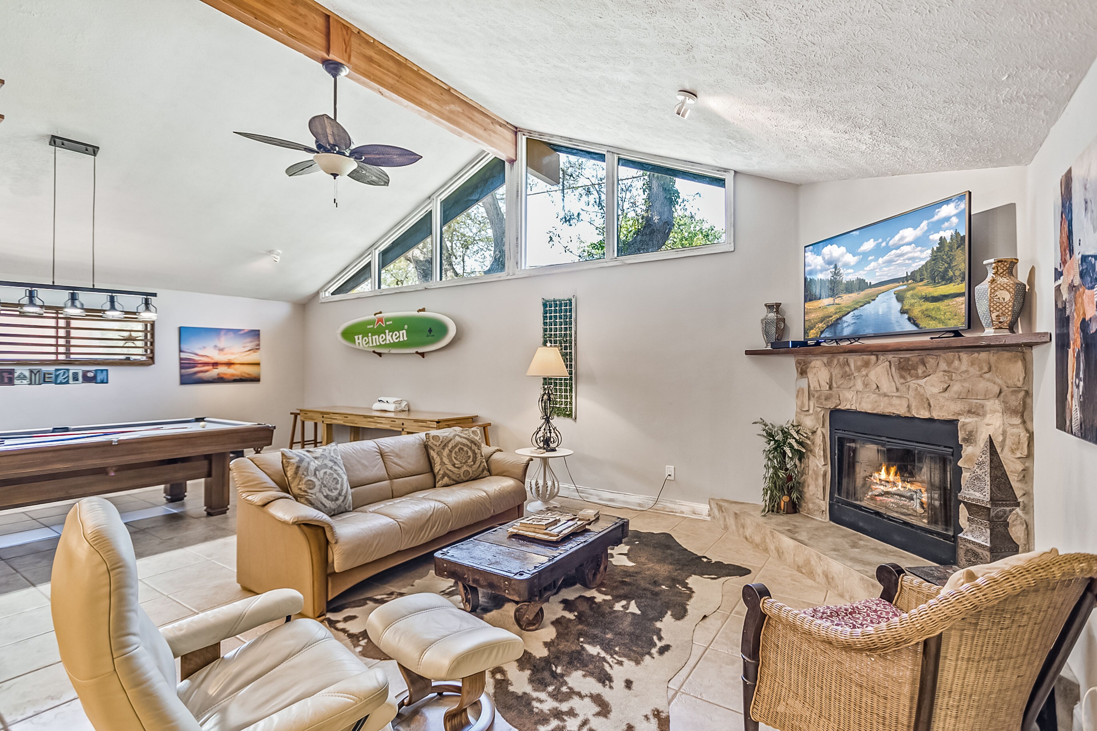A cozy living room with a pool table, leather furniture, a fireplace, and large windows.