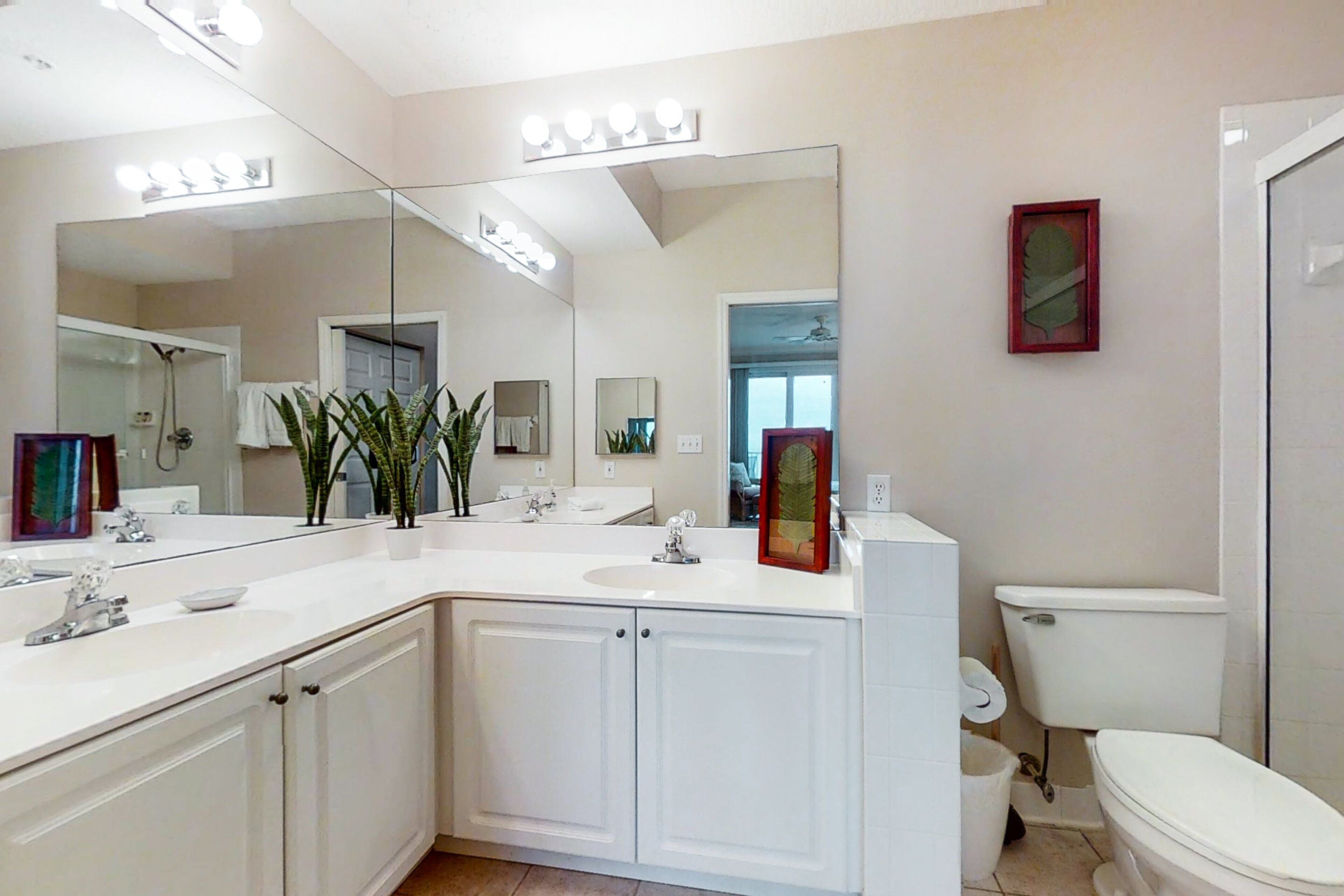Een moderne badkamer met een grote spiegel, witte kastjes en een toilet.