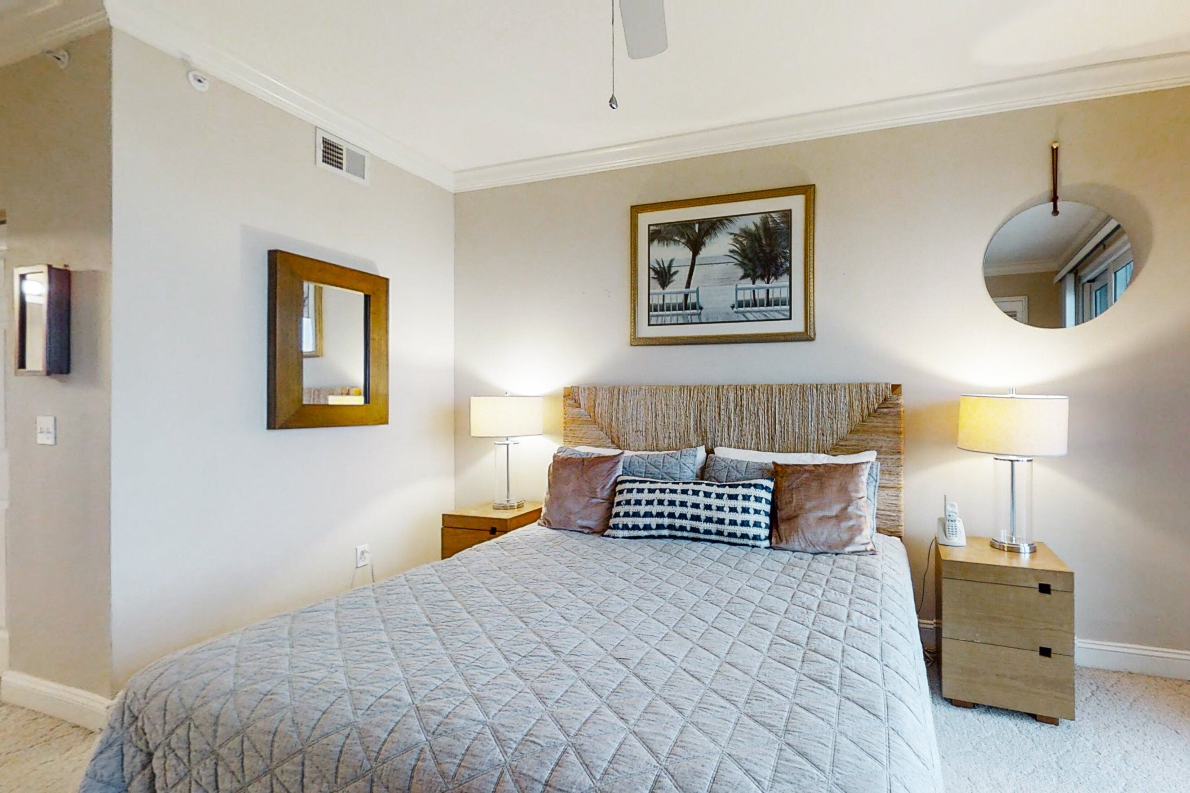 A bedroom with a large bed, two bedside tables, a mirror, and a framed picture on the wall.