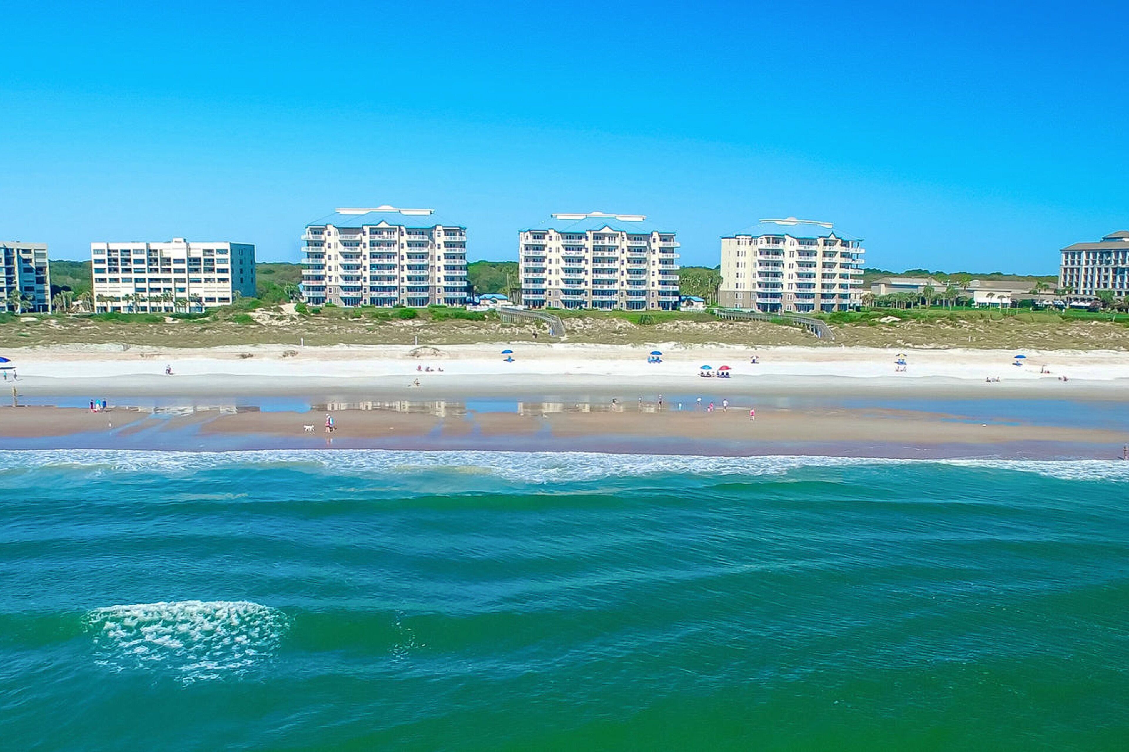 Ett hotell vid stranden med flera höga byggnader, en sandstrand och vågor som slår in mot land.