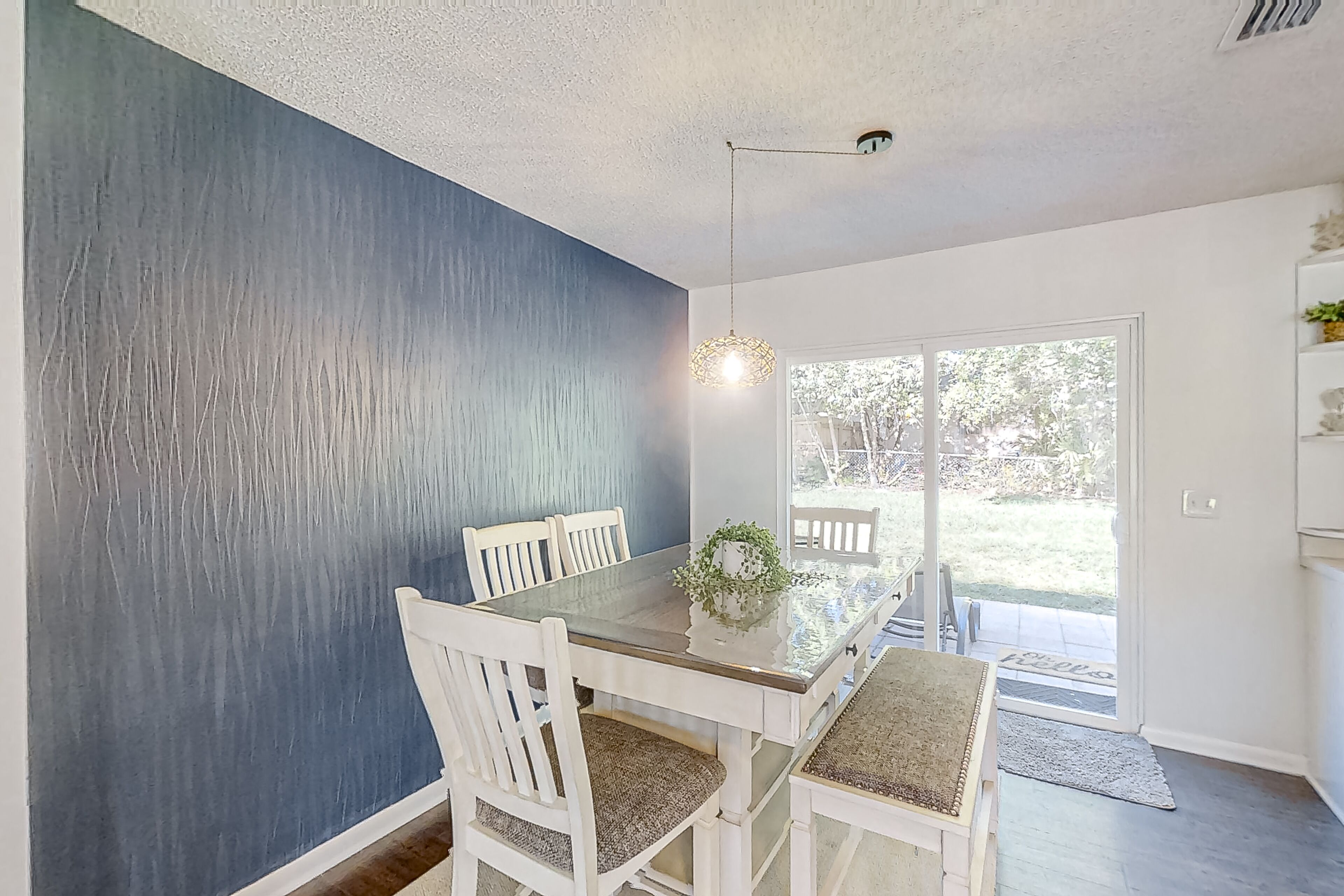 Uma área de refeições com mesa de vidro, cadeiras brancas e uma parede azul de destaque.