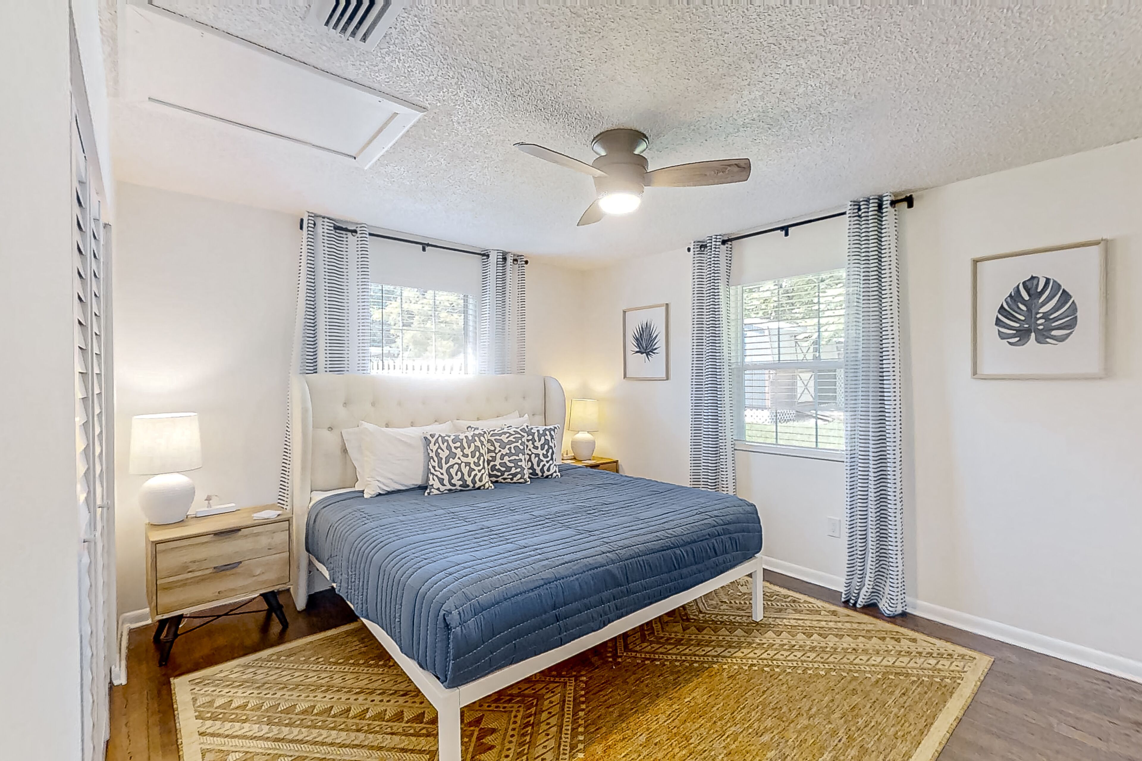 A bedroom with a bed, nightstands, a ceiling fan, and two windows with curtains.