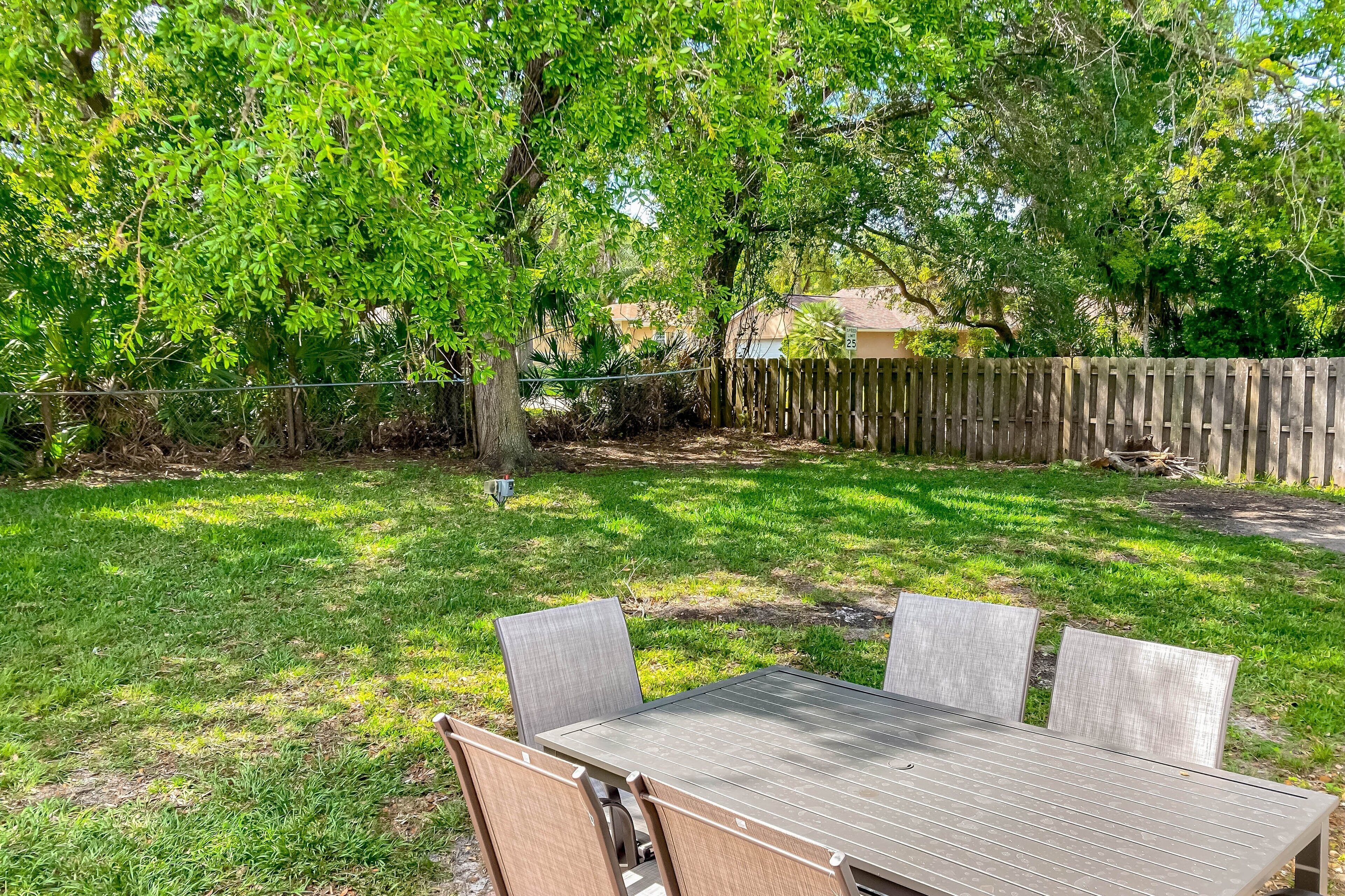 A backyard with a wooden table and chairs, surrounded by a wooden fence and lush greenery.