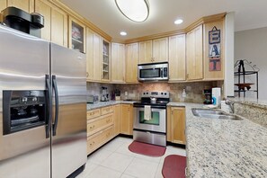 A kitchen with wooden cabinets, stainless steel appliances, granite countertops, and a red rug. - Dog-friendly Vacation Home Close to the Beach With Pool & Screened Porch (St. Augustine)