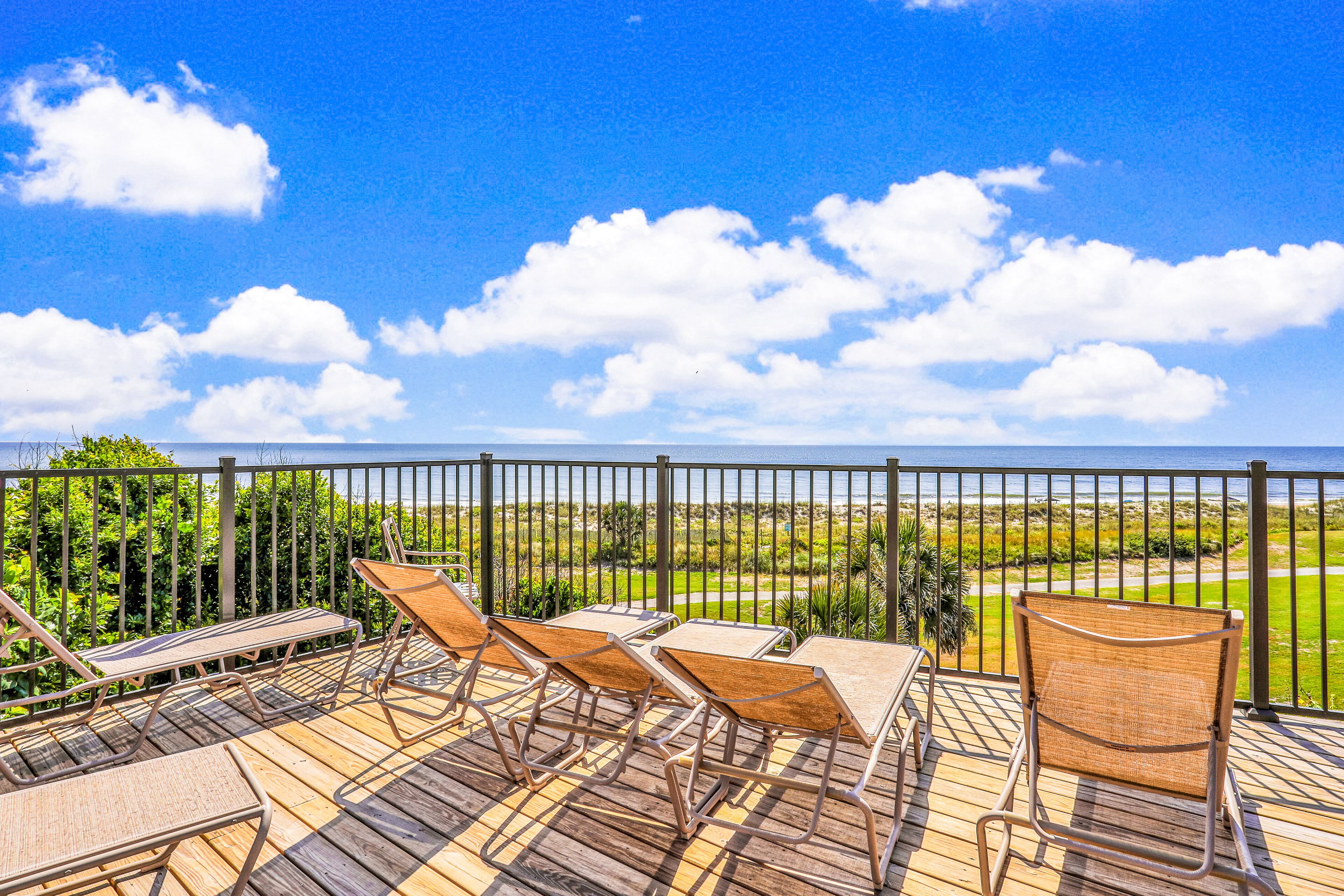 A wooden deck with outdoor furniture, a view of the ocean, and a golf course in the background.
