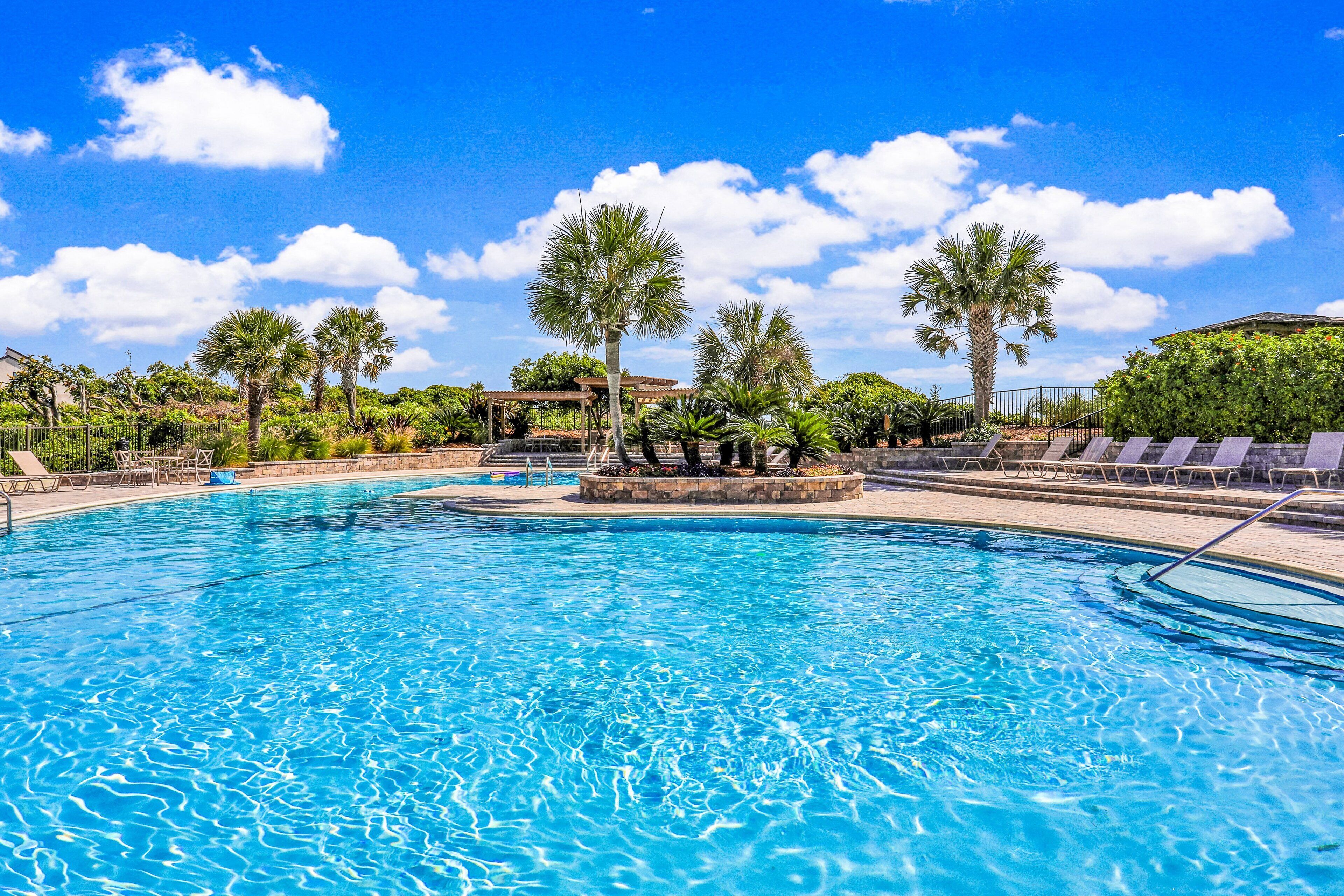 A clear blue pool surrounded by palm trees and lounge chairs.