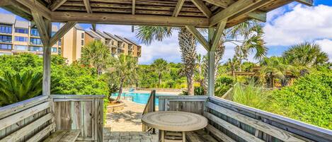 A wooden deck with a table and benches, overlooking a swimming pool and lush greenery.