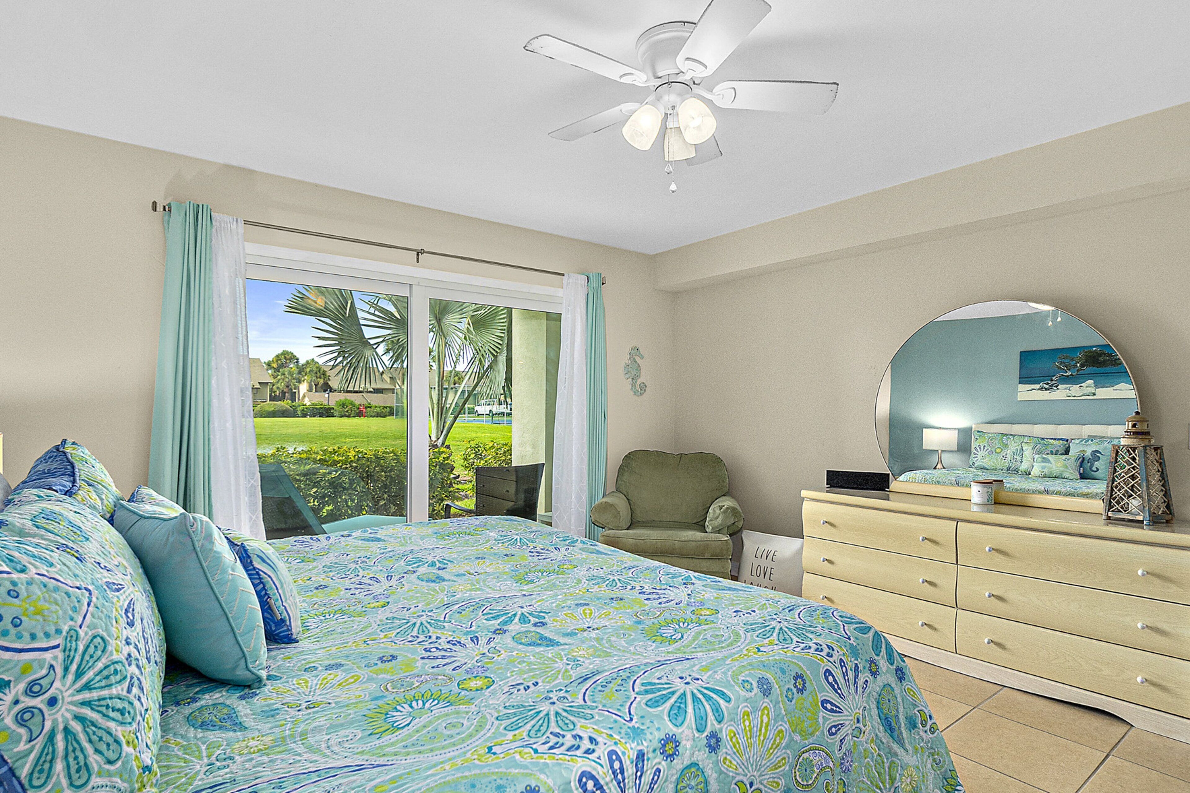 A bedroom with a bed, a dresser, a chair, and a view of a garden through a sliding door.