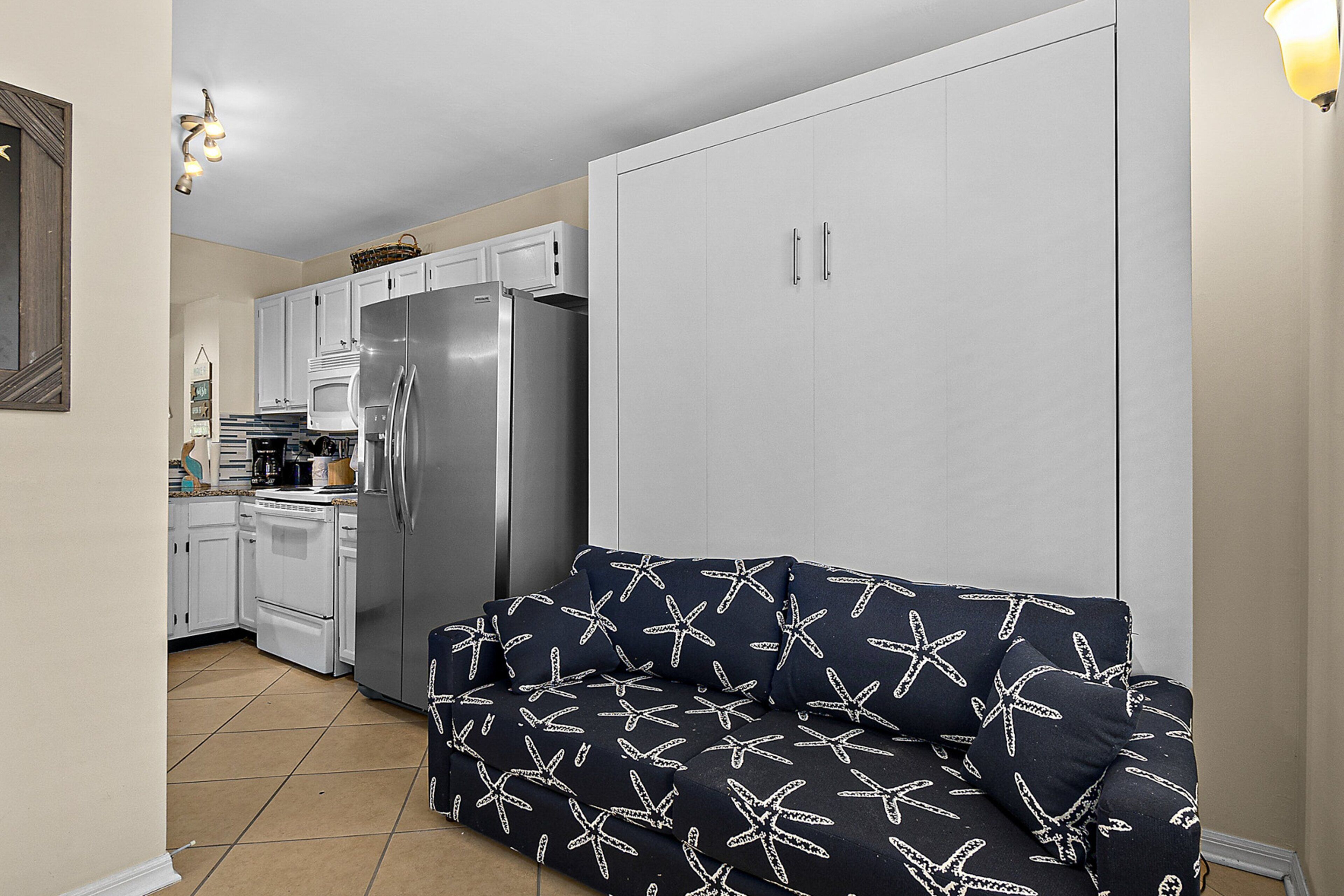 A compact kitchen with white cabinets, a stainless steel refrigerator, and a microwave.