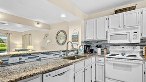 A modern kitchen with white cabinets, a granite countertop, a stainless steel sink, a built-in microwave, and a stove. - Garden-level Condo With Patio, 2 Pools, Gym, Tennis & Sauna - Steps to the Beach (St. Augustine)