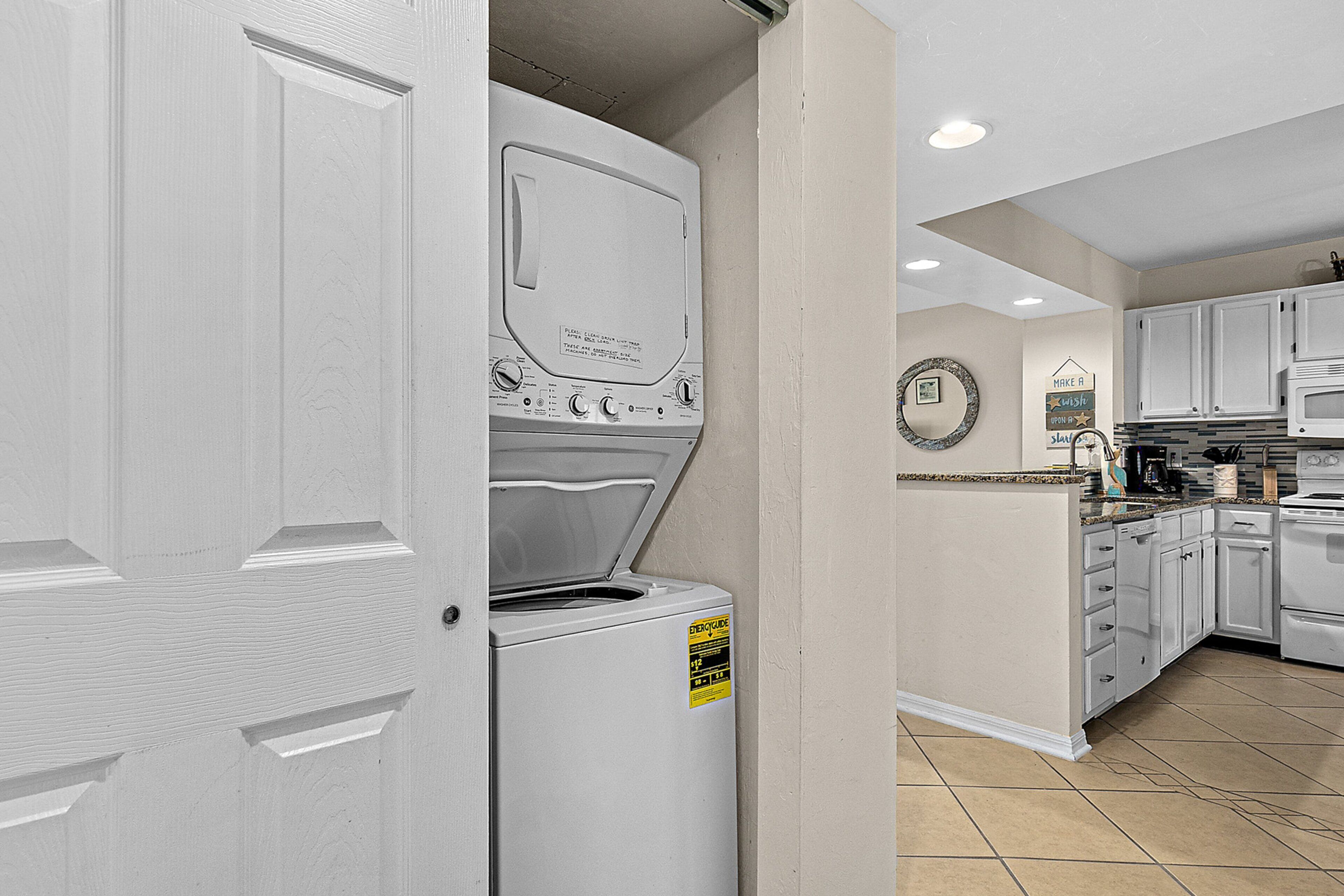 A laundry room with a front-loading washer and dryer, a kitchen area with white cabinets and appliances, and a tiled floor.