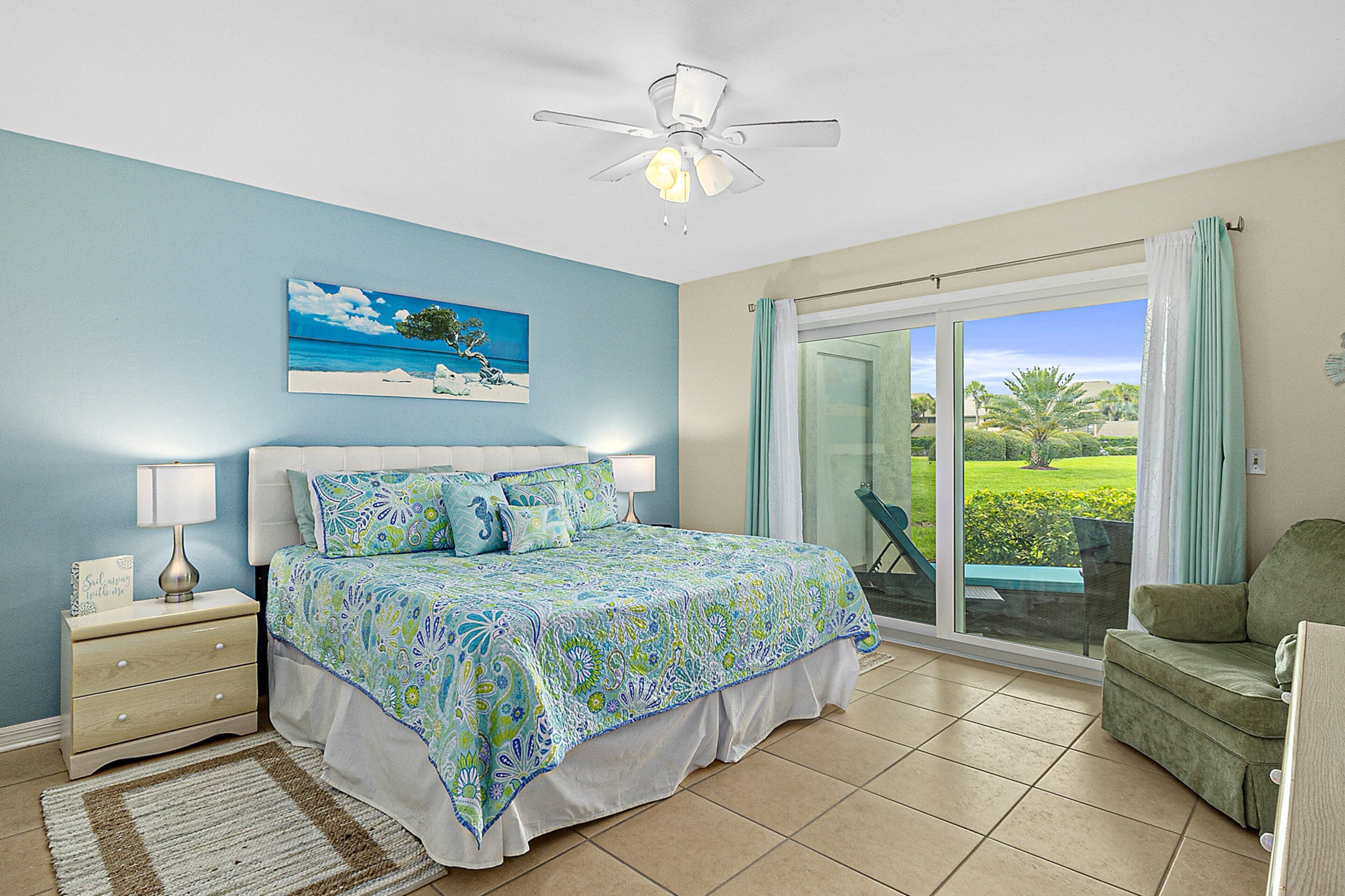 A bedroom with a bed, nightstand, lamp, and a painting of a beach scene.