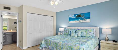 A bedroom with a bed, nightstands, a ceiling fan, a painting, and a bathroom with a sink and mirror.