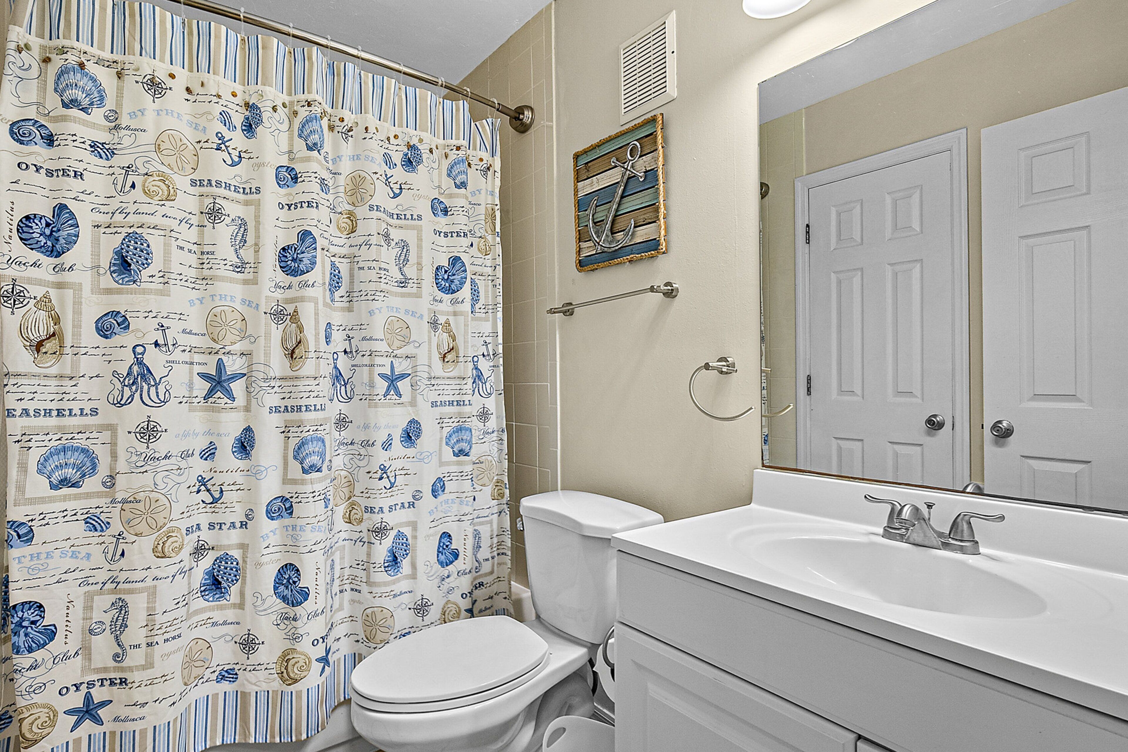 A bathroom with a striped shower curtain, a white toilet, a sink with a mirror, and a towel rack.