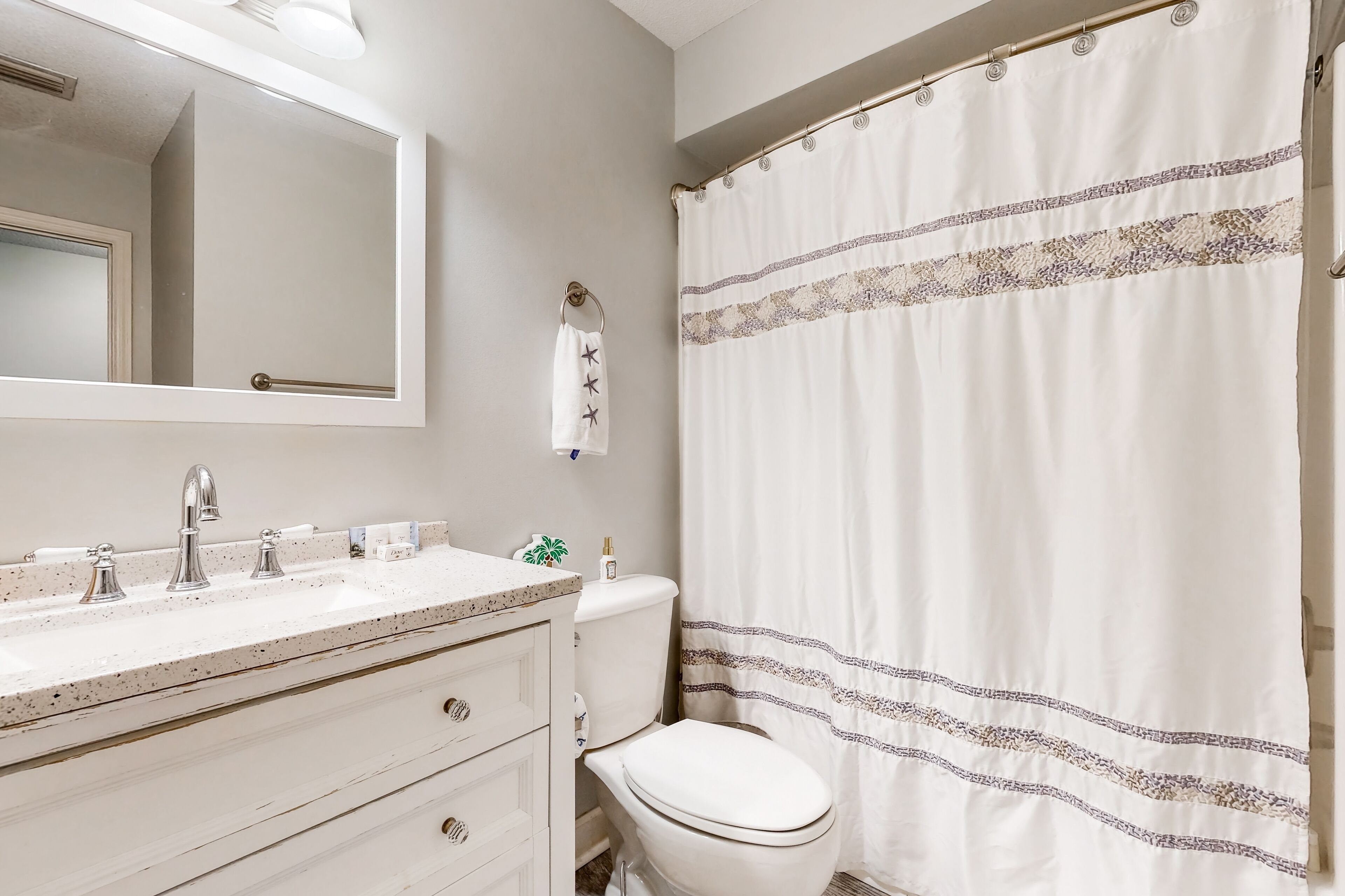 Une salle de bain avec un lavabo blanc, des toilettes et un rideau de douche orné d’une bordure à motifs.