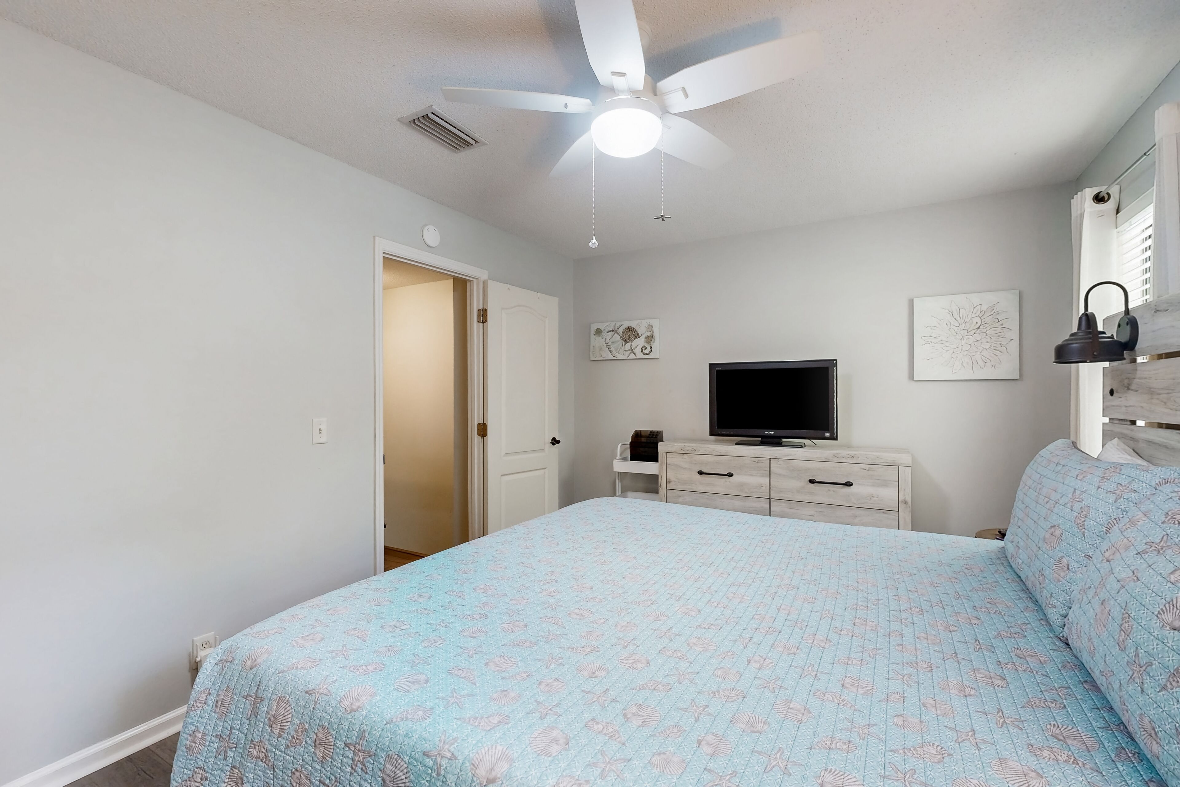 Ein Schlafzimmer mit einem Bett, einem Deckenventilator, einem Fernseher und einer Kommode.
