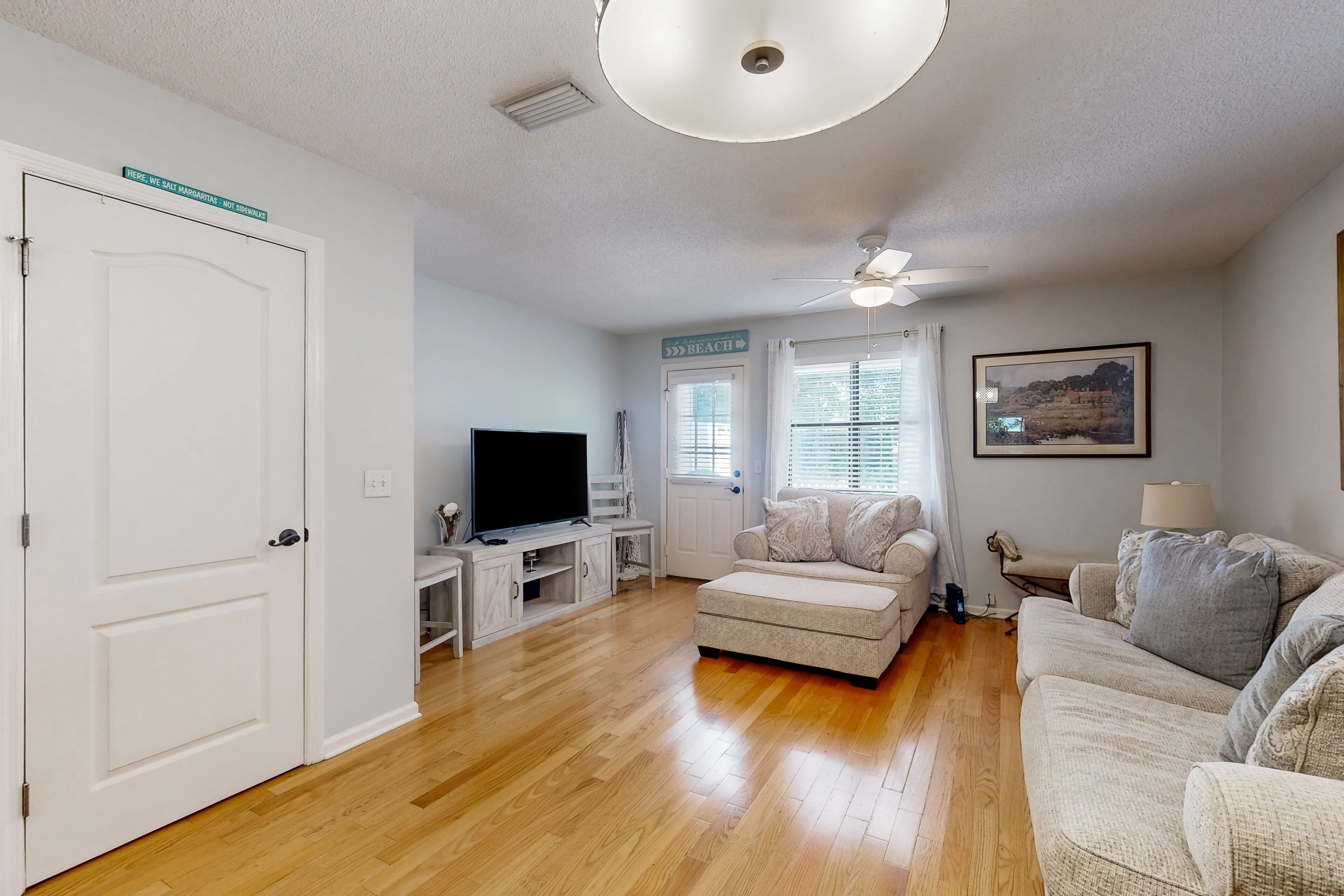 A living room with a television, a ceiling fan, and a sign indicating a beach direction.