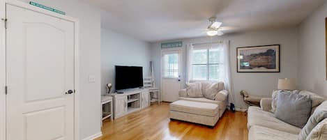 A living room with a television, a ceiling fan, and a sign indicating a beach direction.