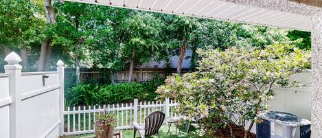 A patio with a white fence, a brick pathway, a lawn, and a large air conditioning unit.