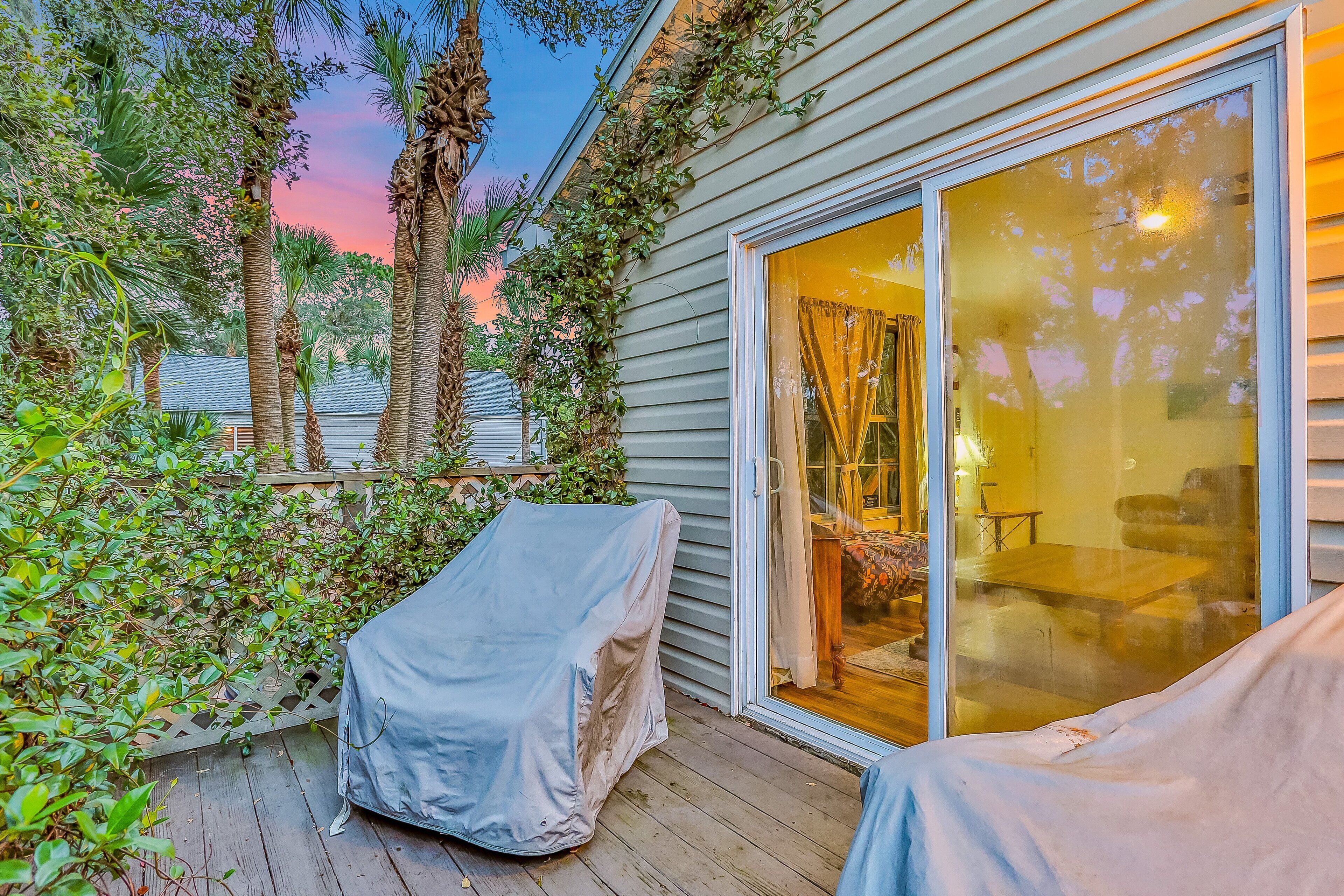 A covered outdoor seating area with a sliding glass door leading to a room with a table and chairs.