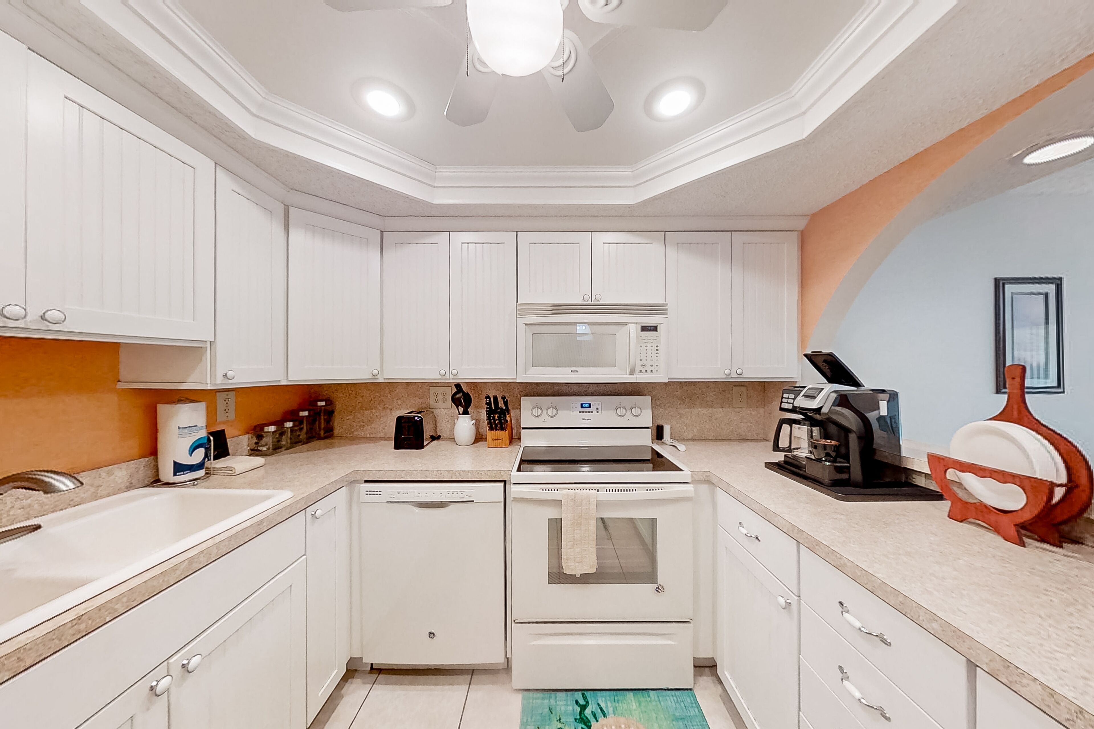 A modern kitchen with white cabinets, a built-in microwave, a stove, and a coffee machine.