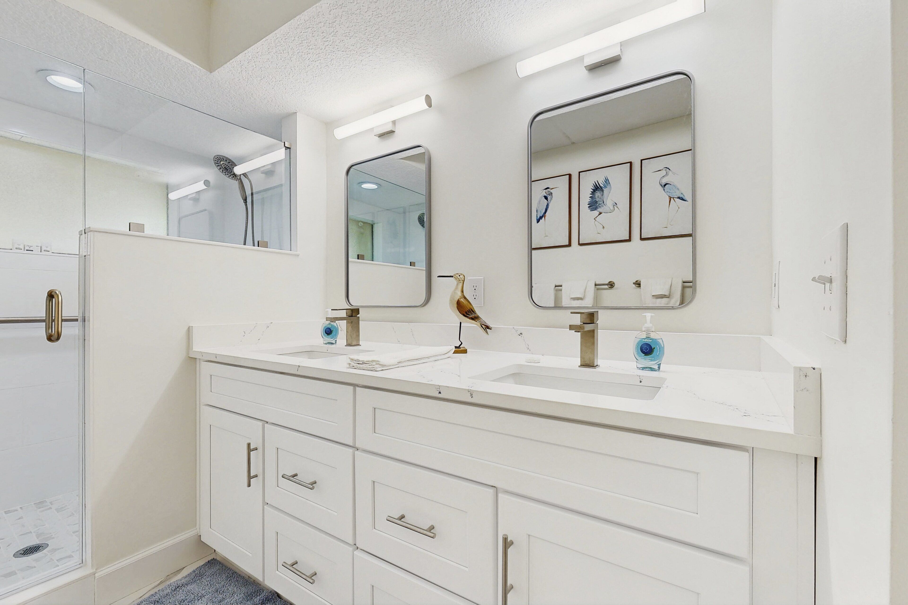 A modern bathroom with two sinks, a glass shower enclosure, and a vanity with drawers.