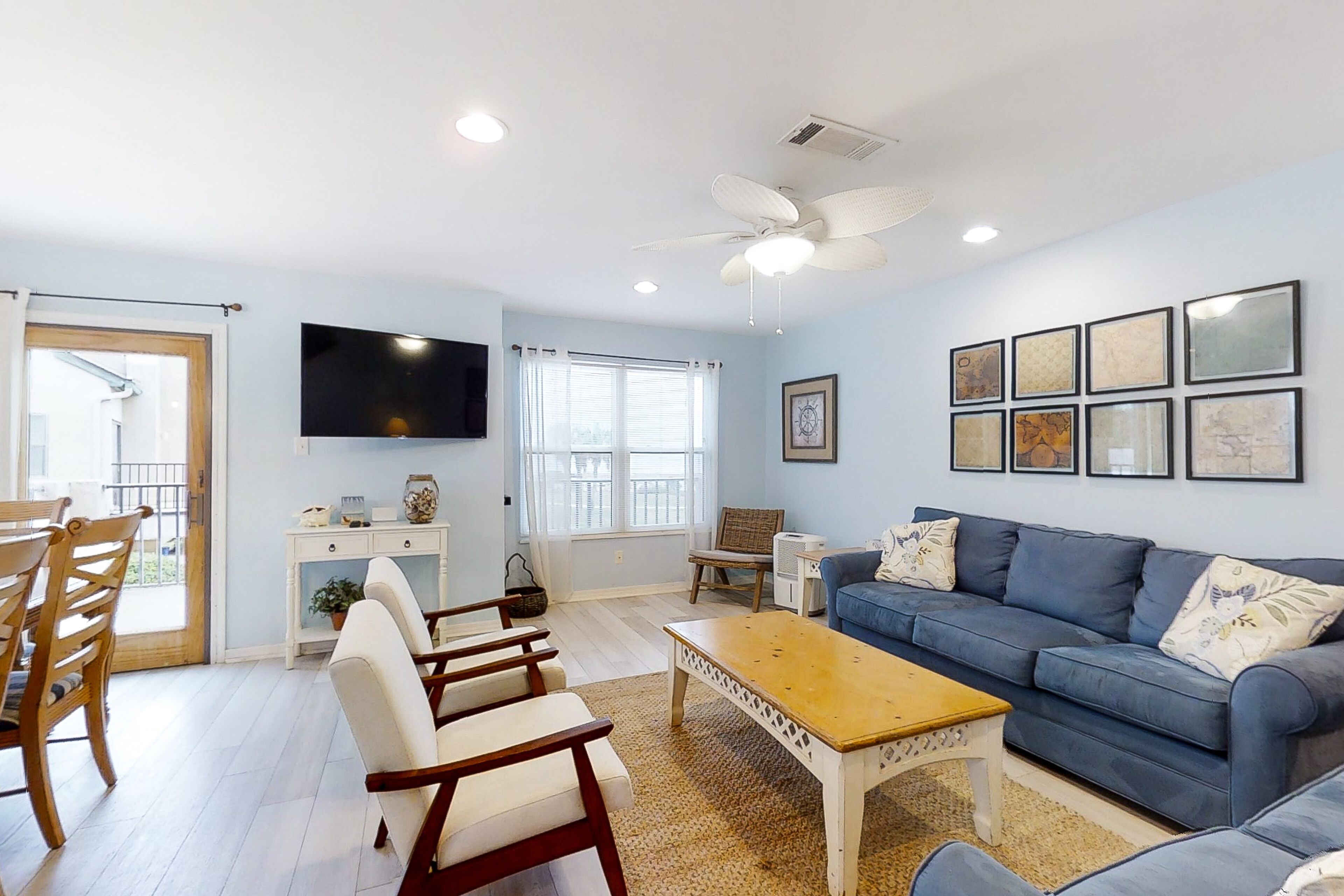 A living room with a blue sofa, wooden chairs, a coffee table, a flat-screen TV, and framed artwork on the wall.