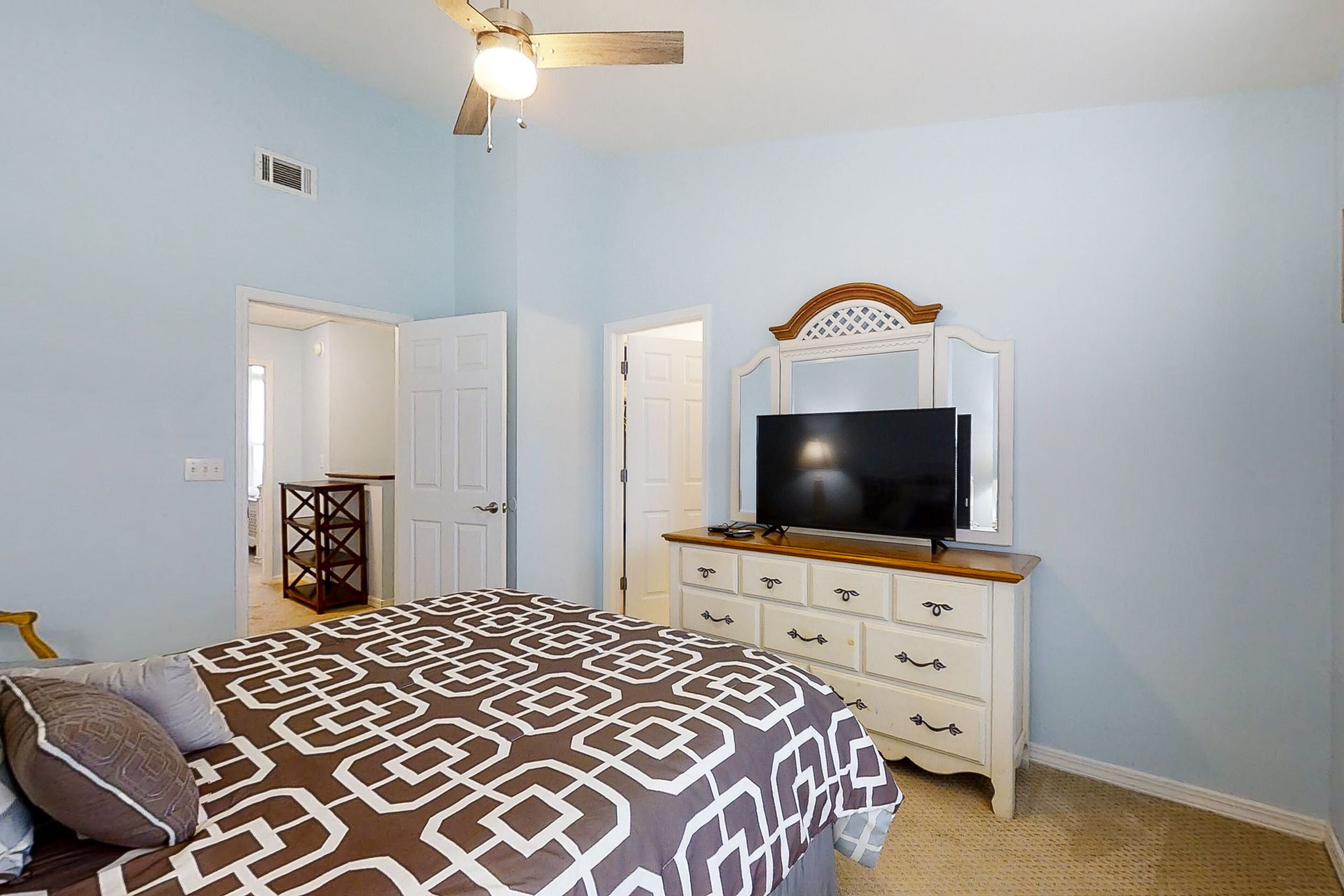 Une chambre à coucher avec un lit, une commode sur laquelle se trouve un téléviseur et un ventilateur de plafond.