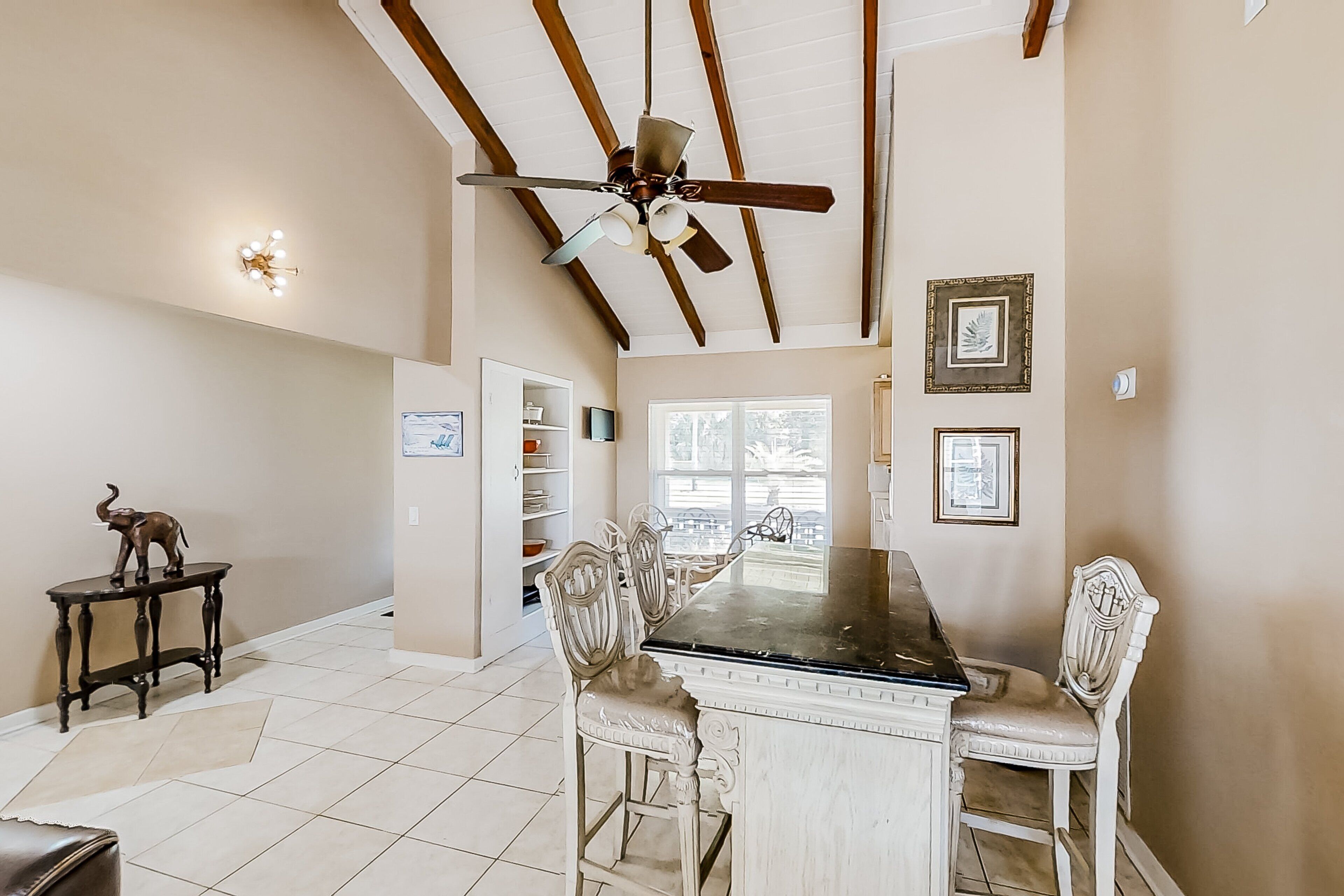A dining area with a wooden table, white chairs, a ceiling fan, and framed pictures on the wall.