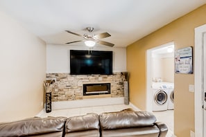 Una sala de estar con chimenea de piedra, televisor de pantalla plana, ventilador de techo y sofá.
