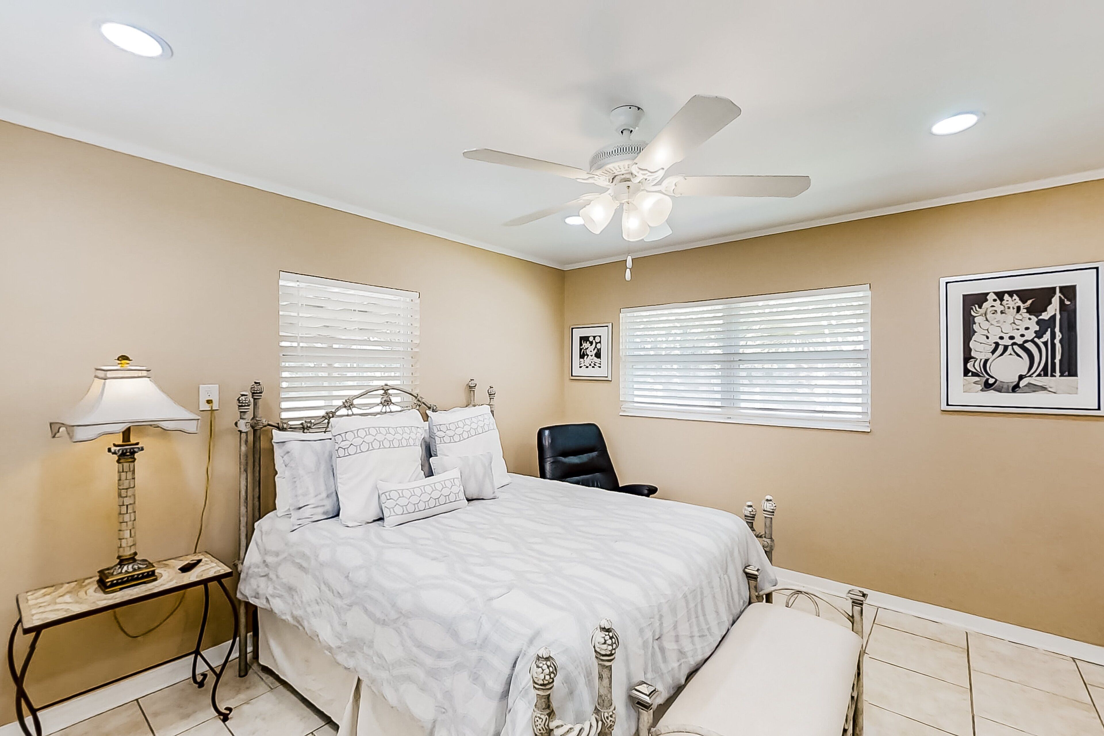 A bedroom with a bed, a chair, a nightstand, a lamp, and a ceiling fan.