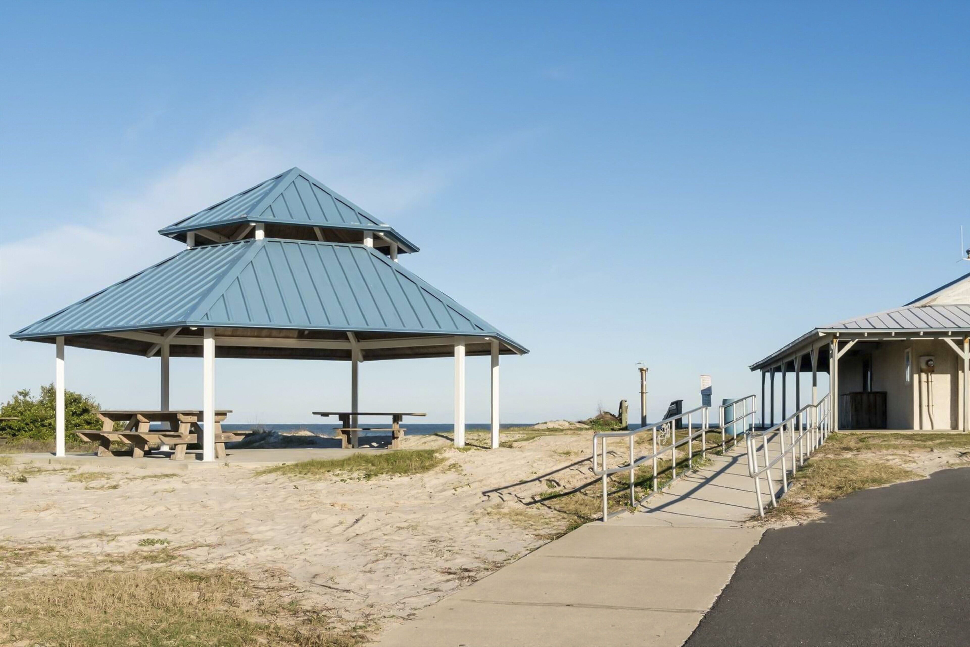 A beach pavilion with a metal roof, picnic tables, and a wheelchair-accessible ramp.