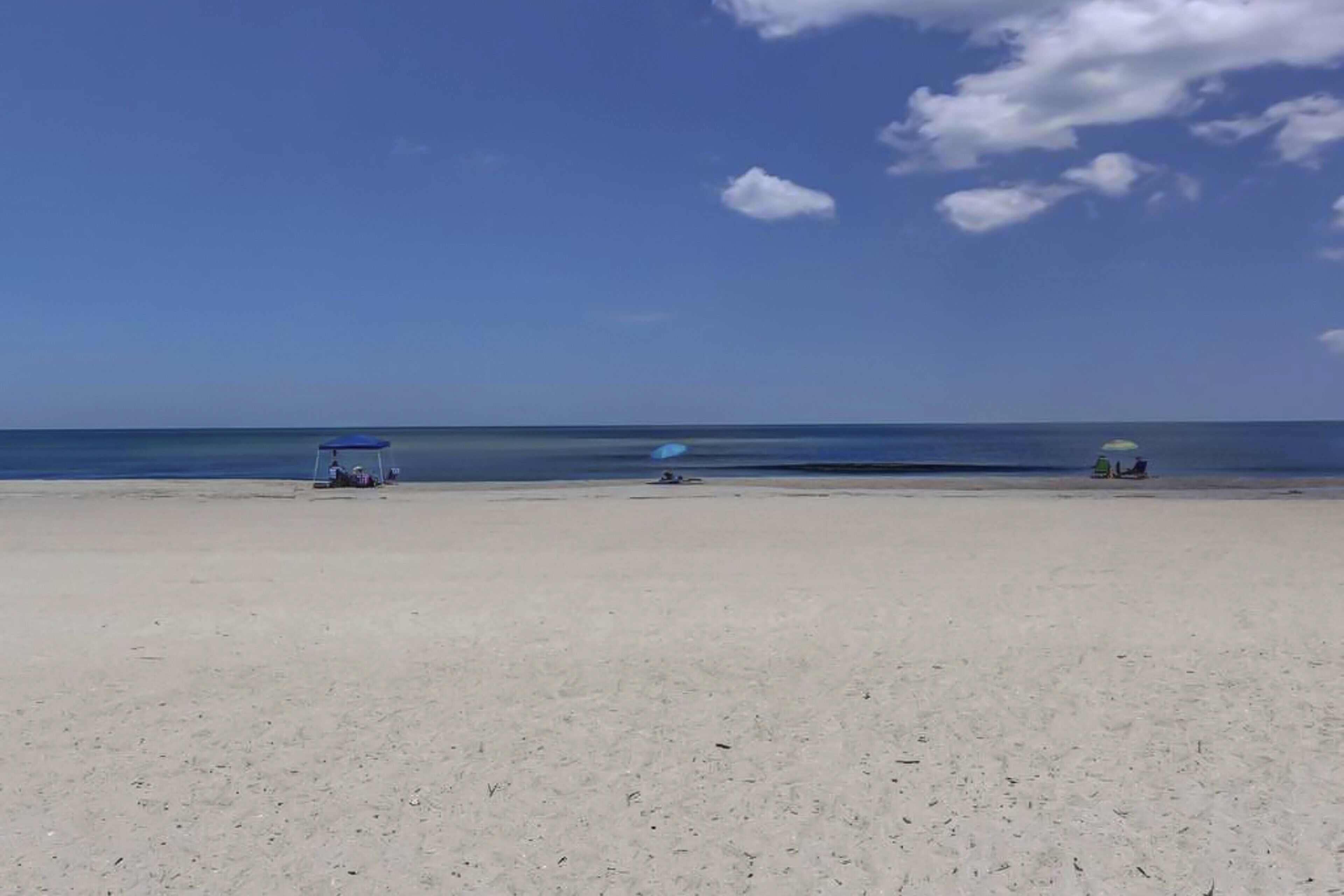 A beach with a clear sky, calm sea, and a few beach umbrellas.