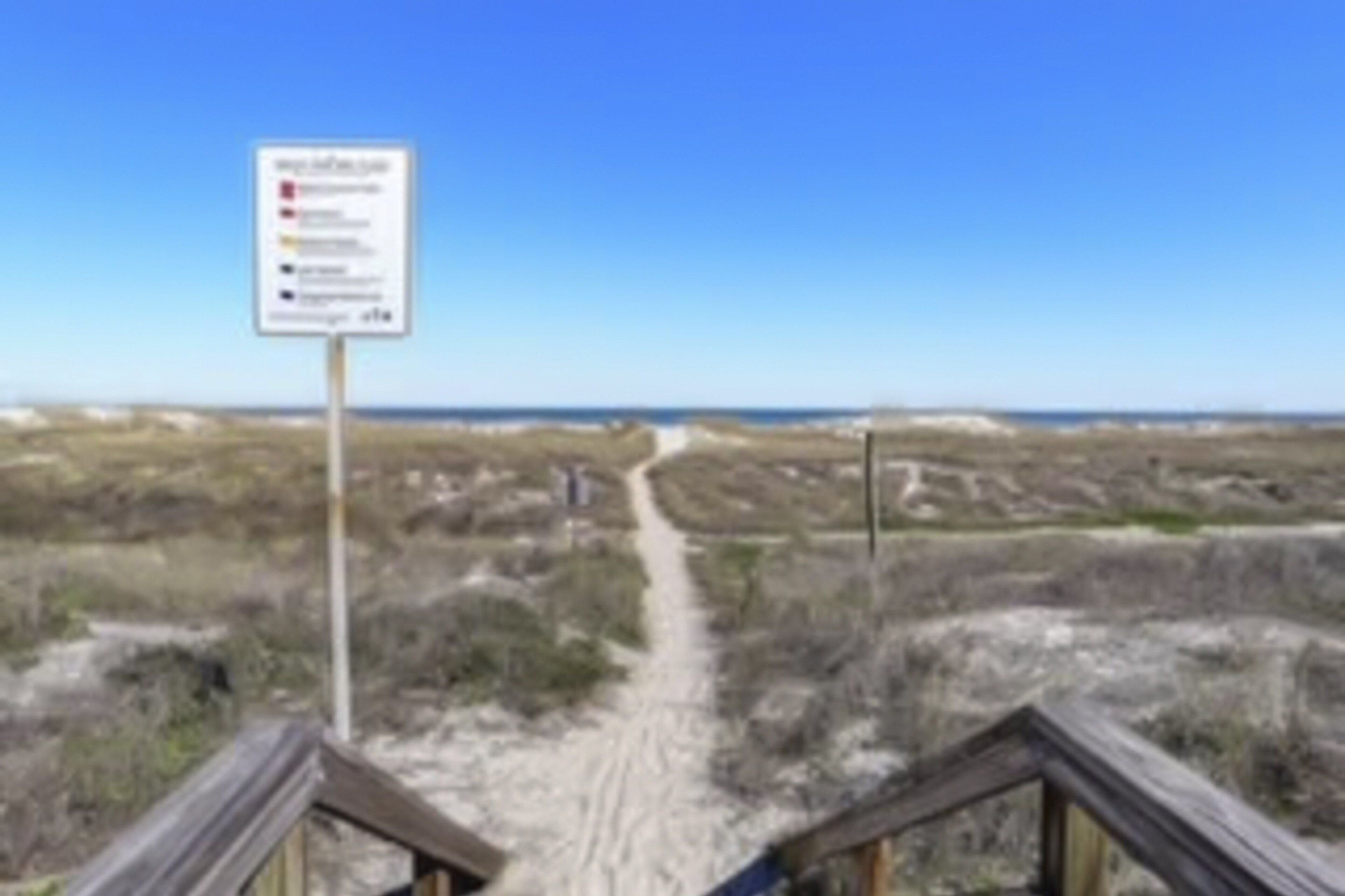 A wooden boardwalk leading to a beach with a sign indicating amenities and rules.