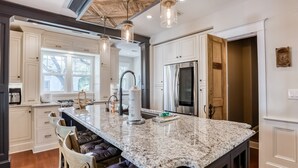 Una cocina con armarios blancos, una isla de granito y electrodomésticos de acero inoxidable.