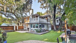 A two-story house with a covered patio, a fire pit, and a well-maintained lawn. - Extraordinary Old Florida Home With Designer Interior & Backyard Treehouse (St. Augustine)