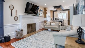 Una sala moderna con chimenea, televisor y cocina al fondo.