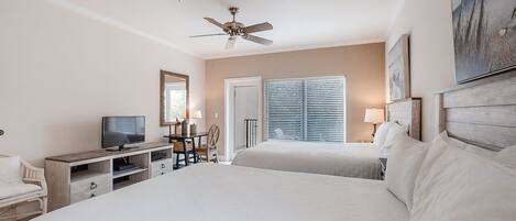 A hotel room with a large bed, a TV, a desk, and a ceiling fan.