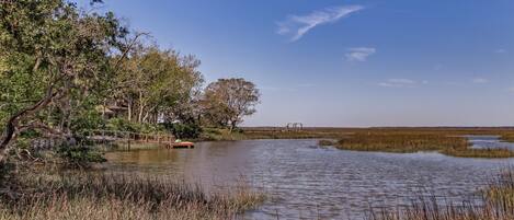 A calm river with a wooden bridge, surrounded by trees and marshland.